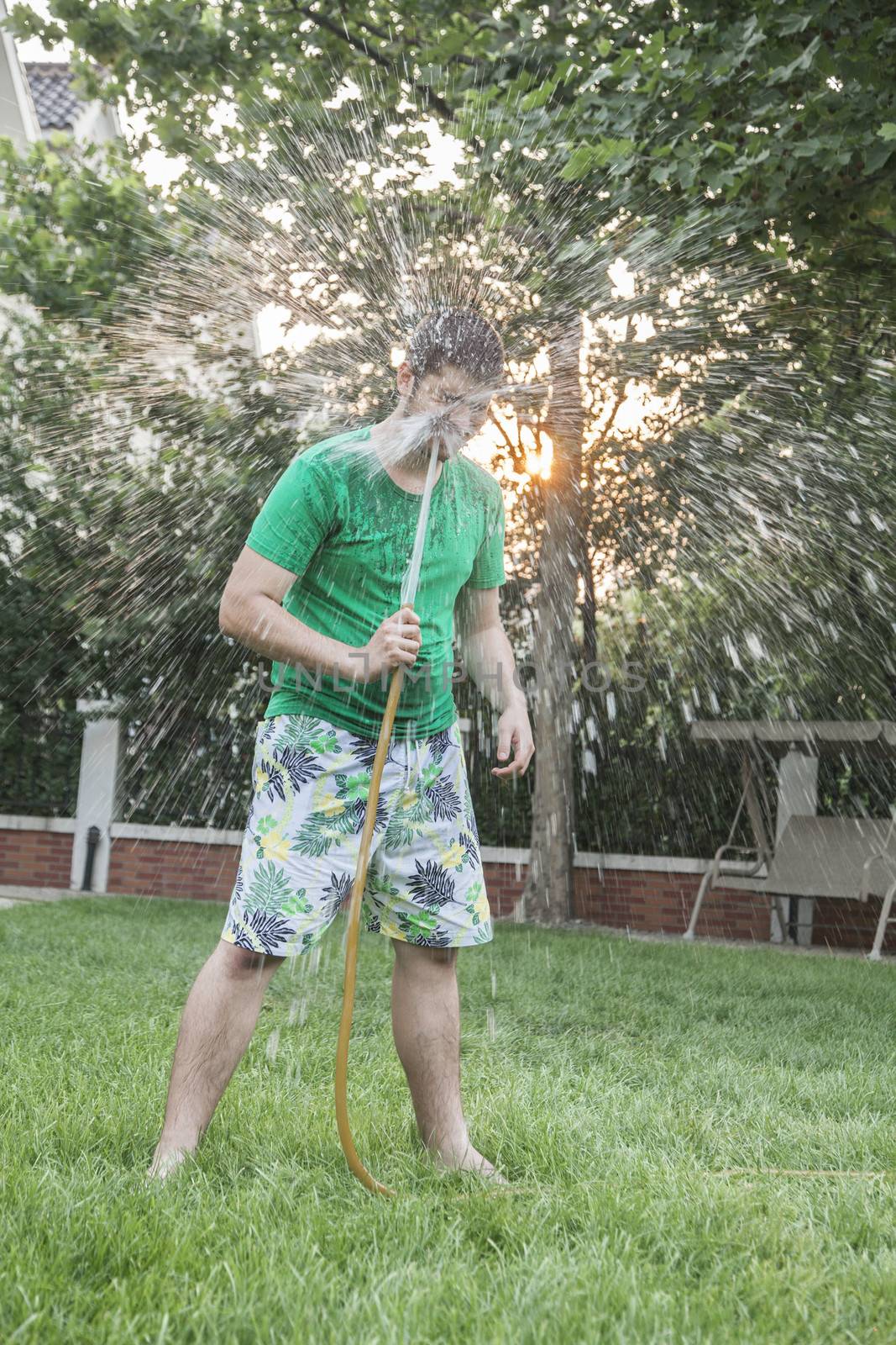 Young man spraying himself with a garden hose in the face, outdoors in the garden