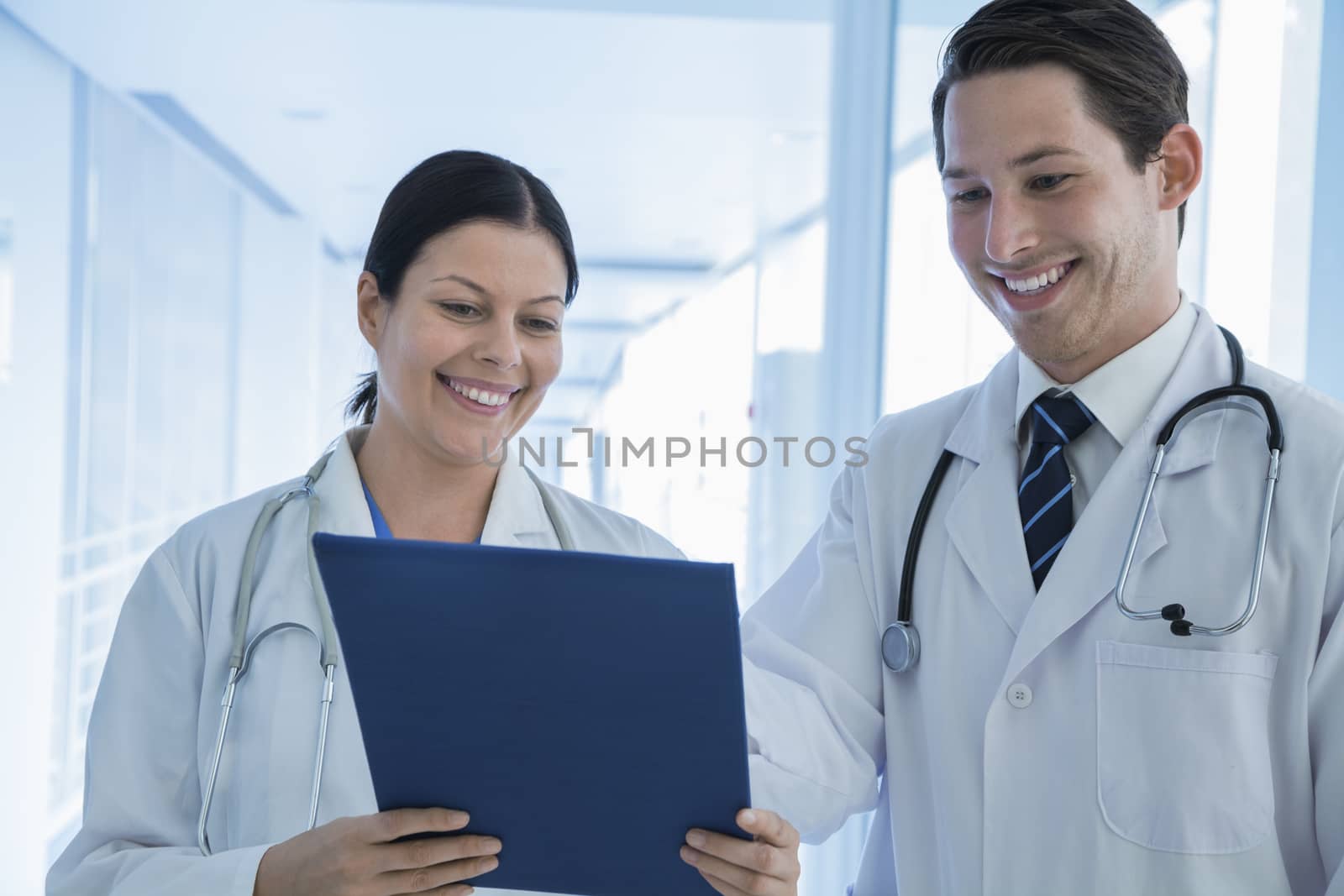 Two smiling doctors looking down at a medical record in the hospital by XiXinXing