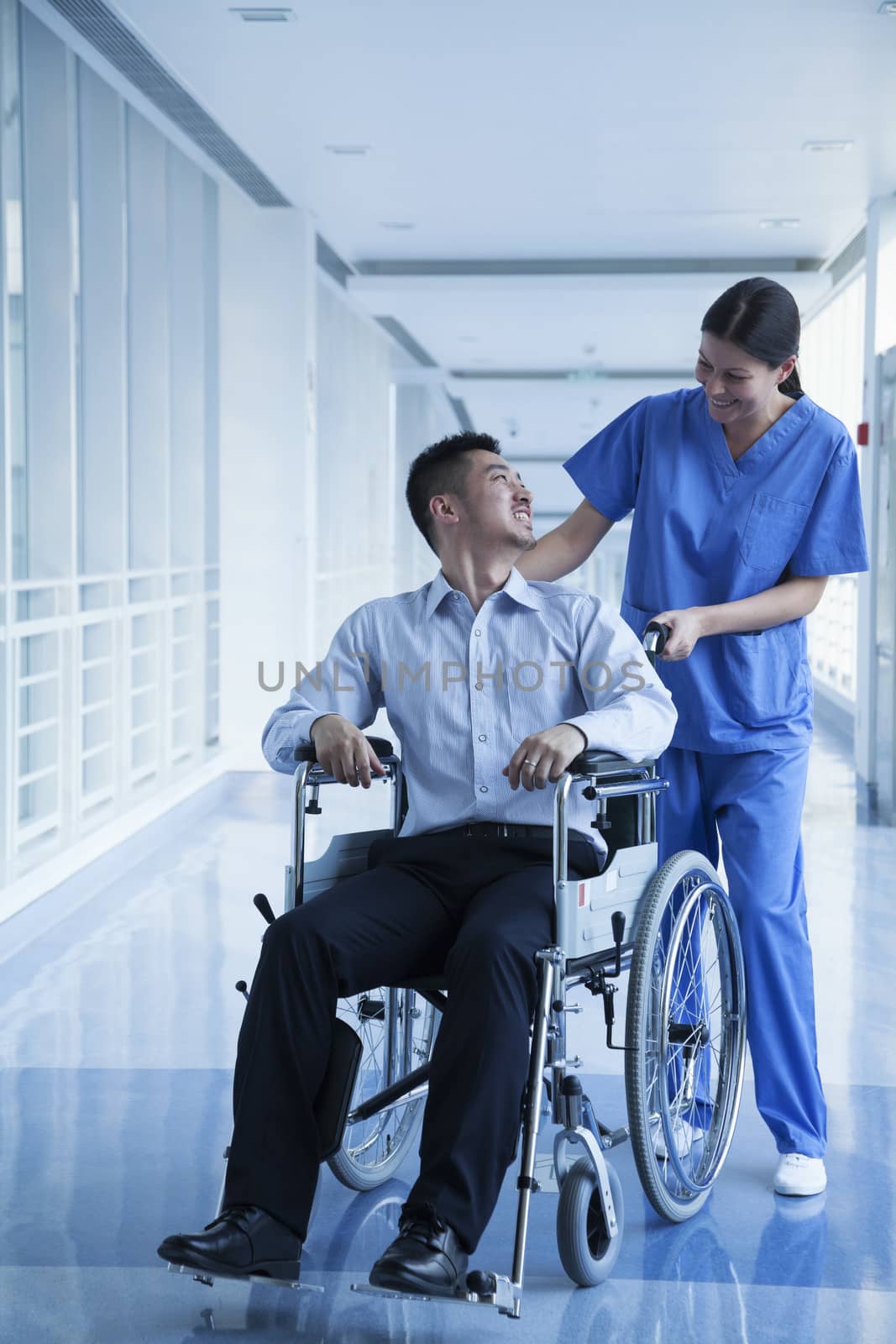 Smiling female nurse pushing and assisting patient in a wheelchair in the hospital 