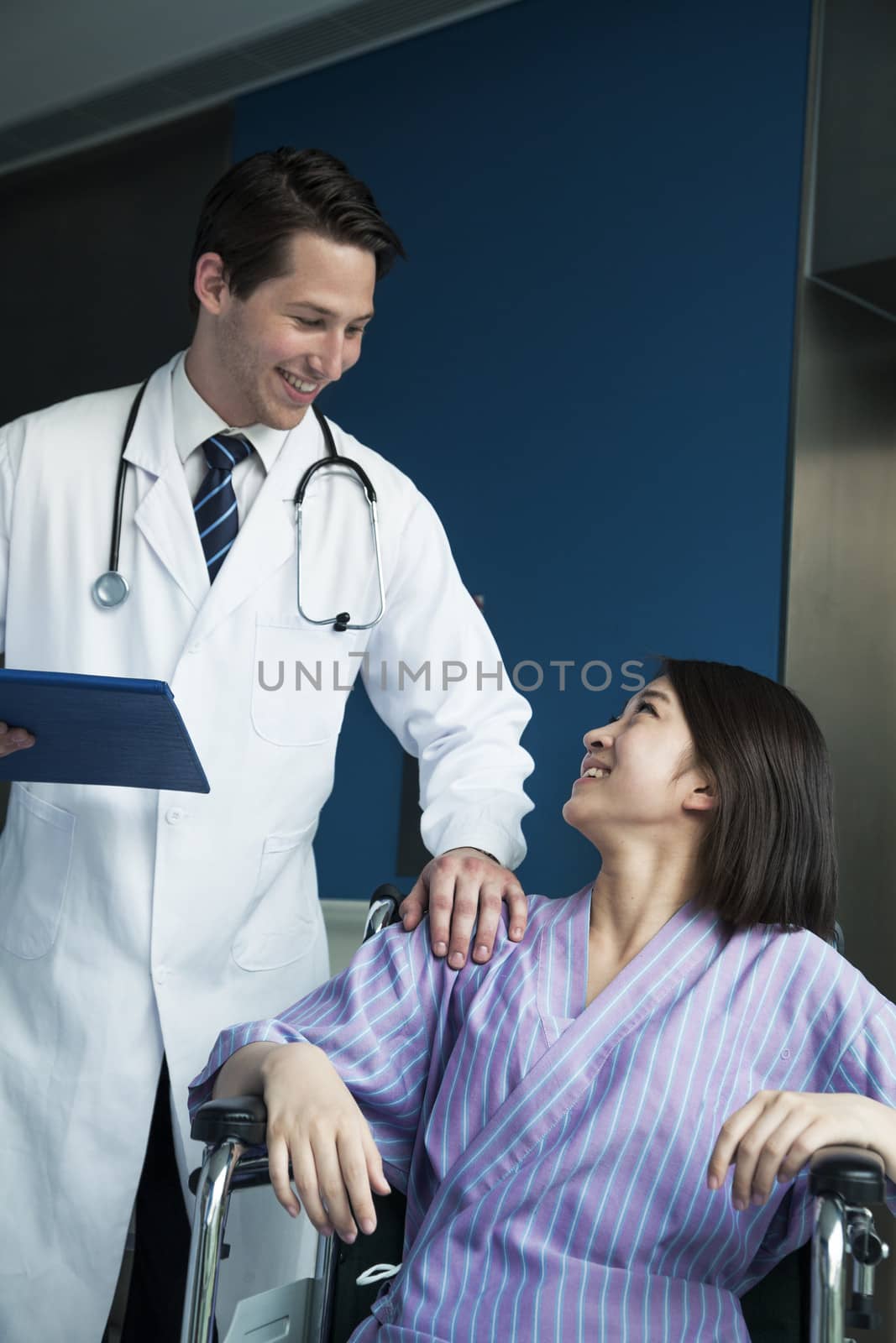 Young smiling female patient sitting in a wheelchair, looking up at doctor standing beside her