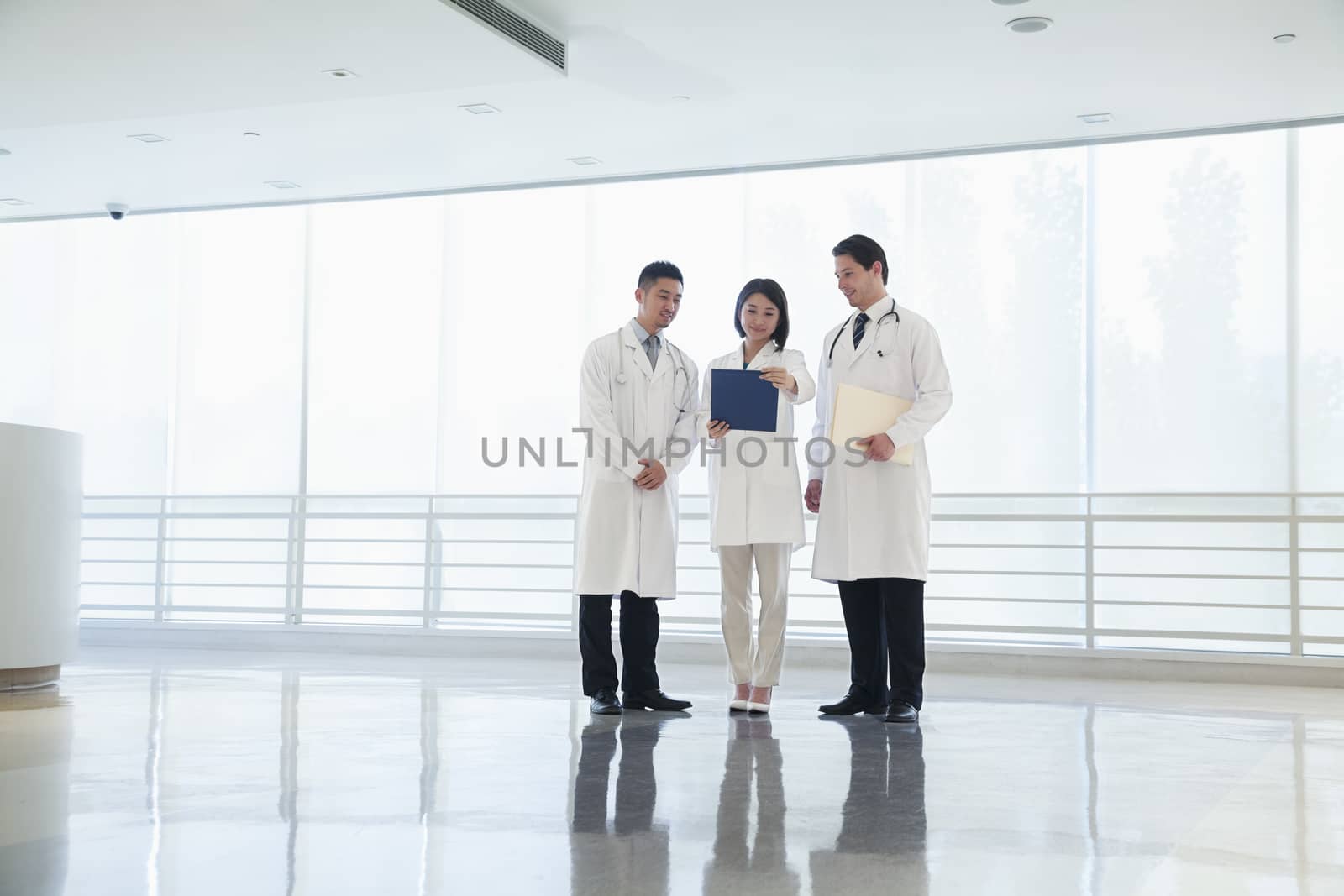 Three doctors standing and looking down at a document in the hospital, full length