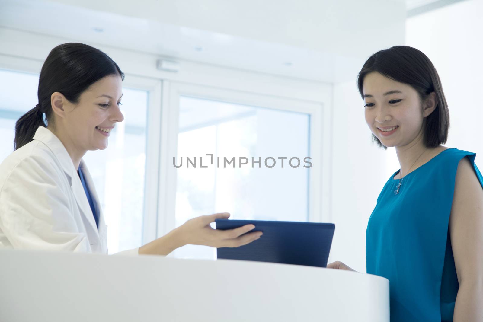 Smiling doctor and patient standing by the counter in the hospital looking down at medical record