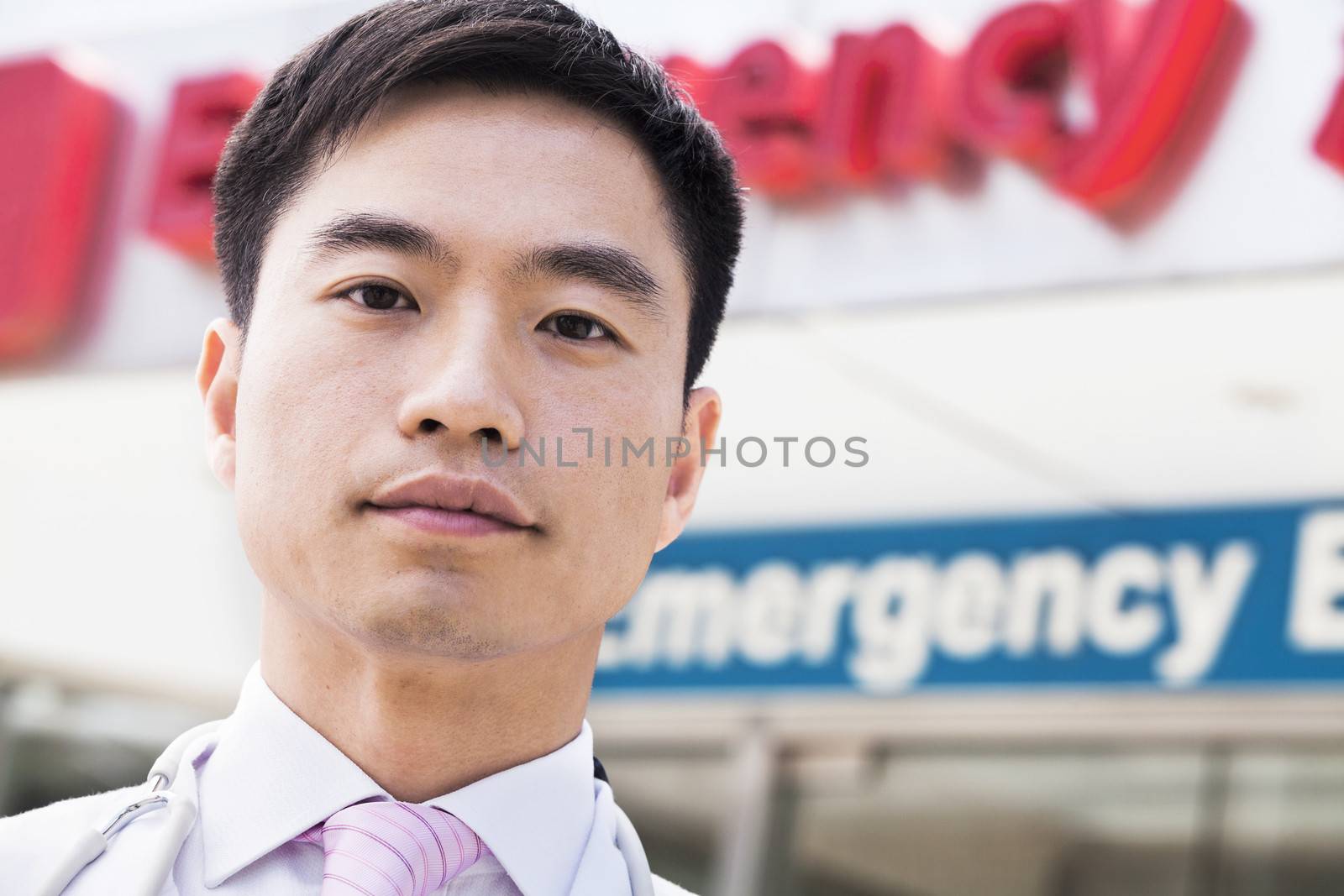 Portrait of smiling doctor outside of the hospital, emergency room sign in the background, Close-Up