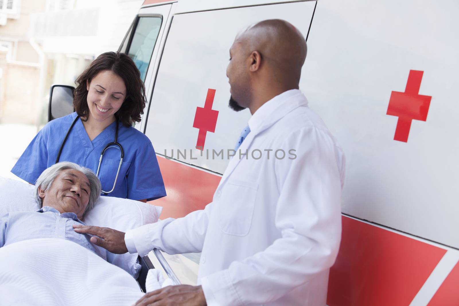 Doctor and paramedic wheeling in a elderly patient on a stretcher in front of an ambulance by XiXinXing