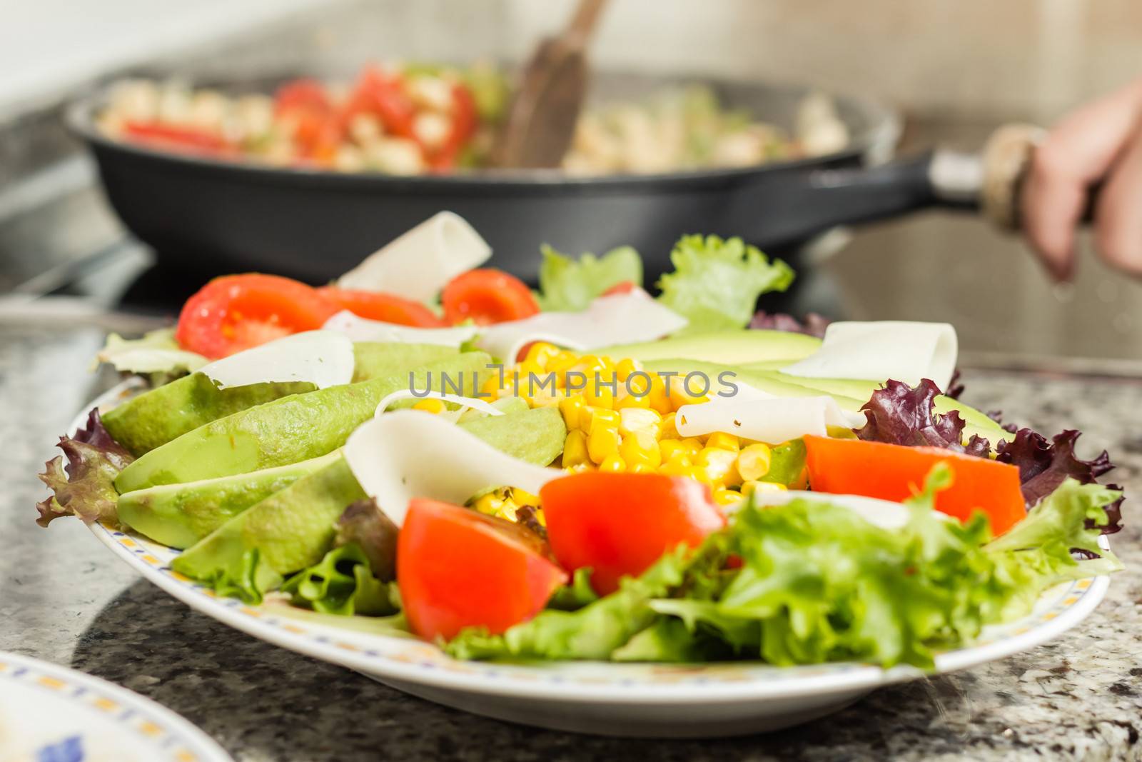 Closeup of fresh salad dish and female cooking in a black pan in the background