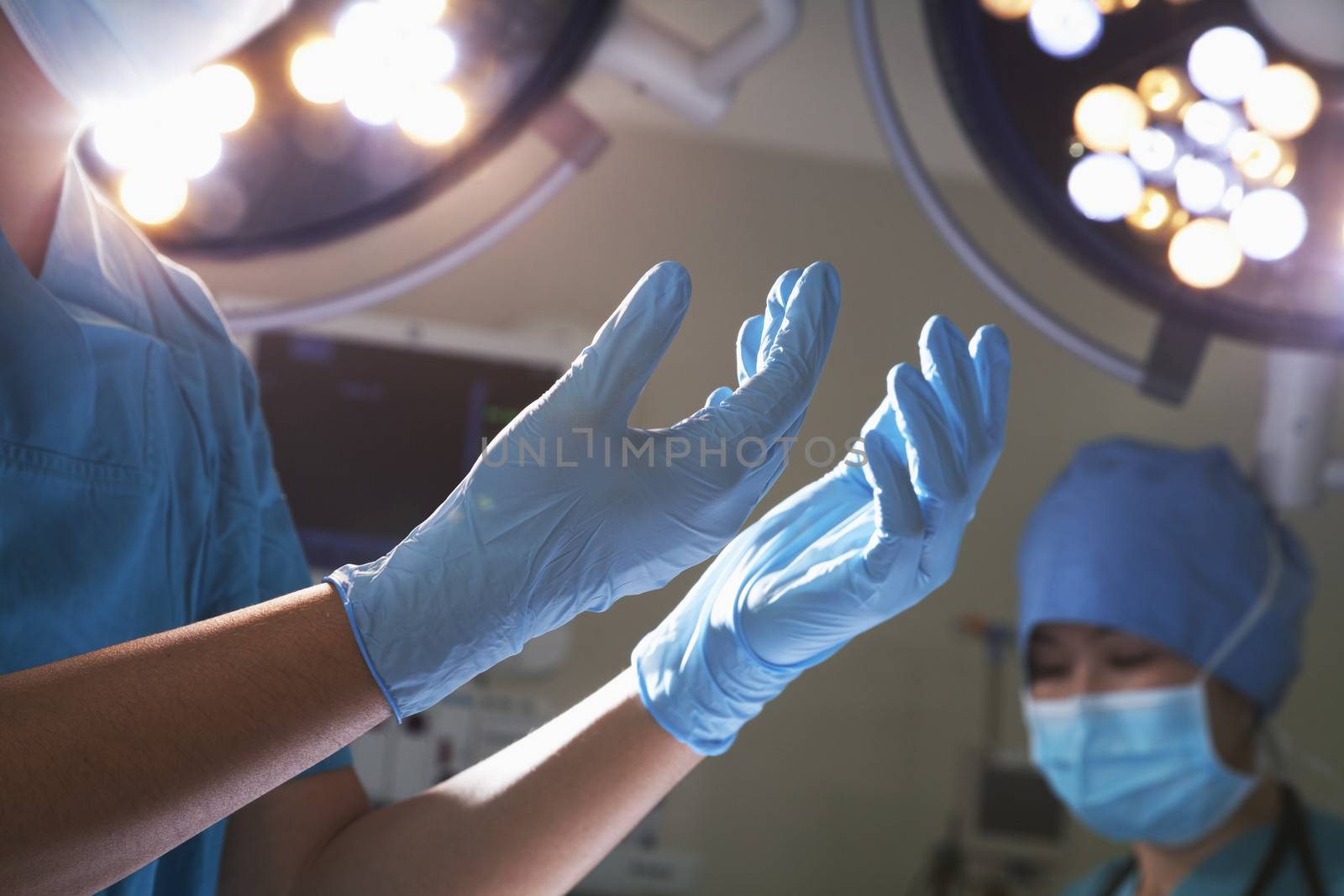 Midsection view of hands in surgical gloves and surgical lights in the operating room  by XiXinXing