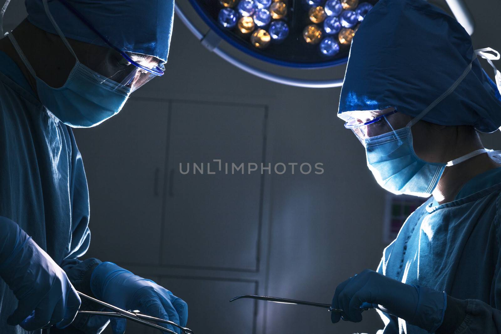Two surgeons looking down and working at the operating table, dark operating room