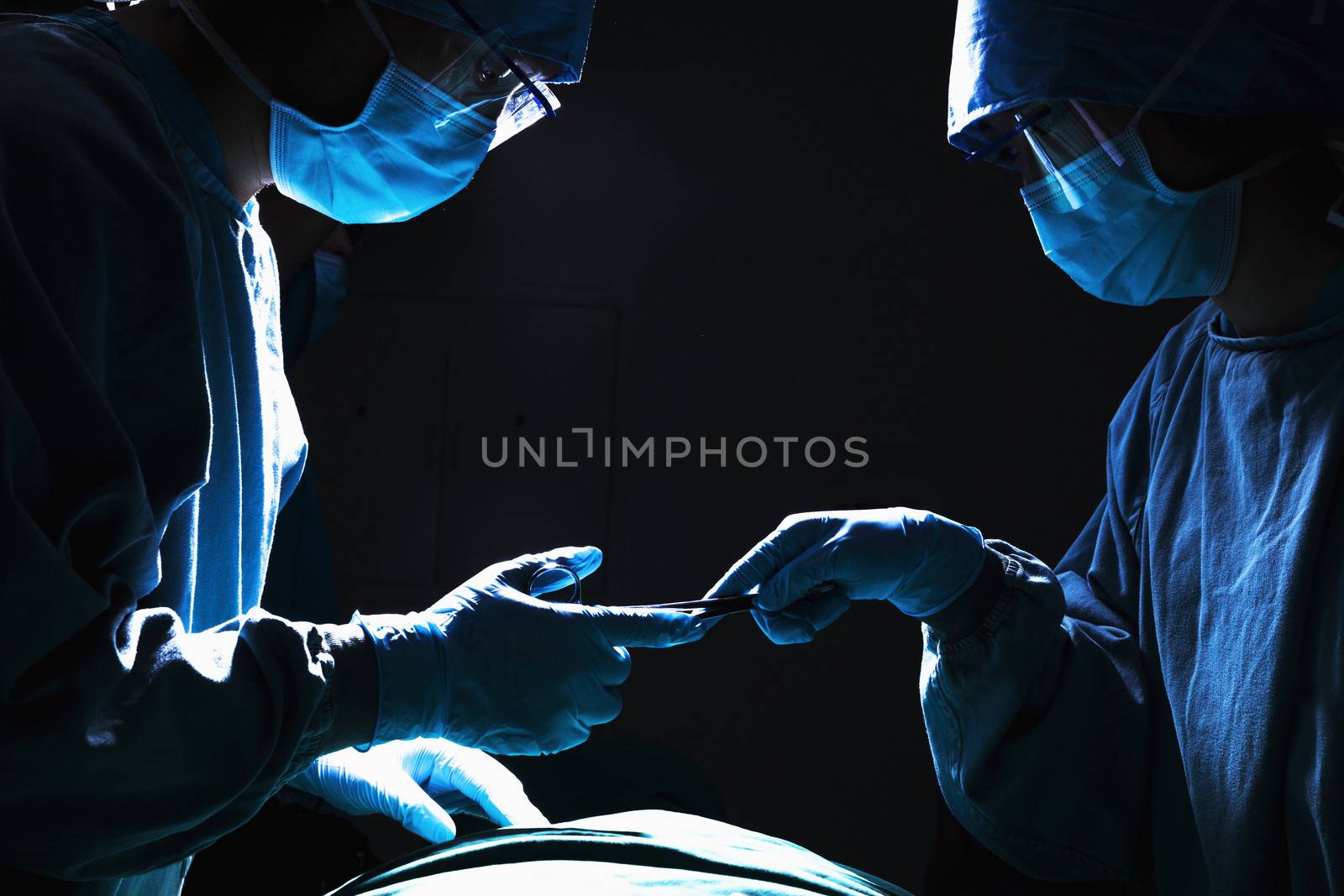 Two surgeons working and passing surgical equipment in the operating room, dark  by XiXinXing