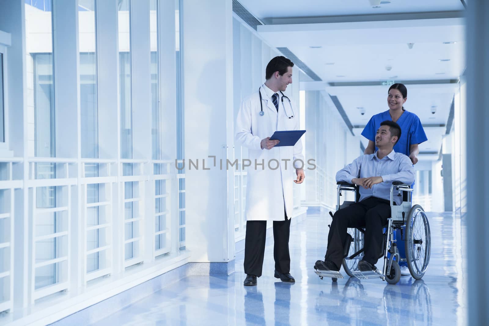 Smiling female nurse pushing and assisting patient in a wheelchair in the hospital, talking to doctor