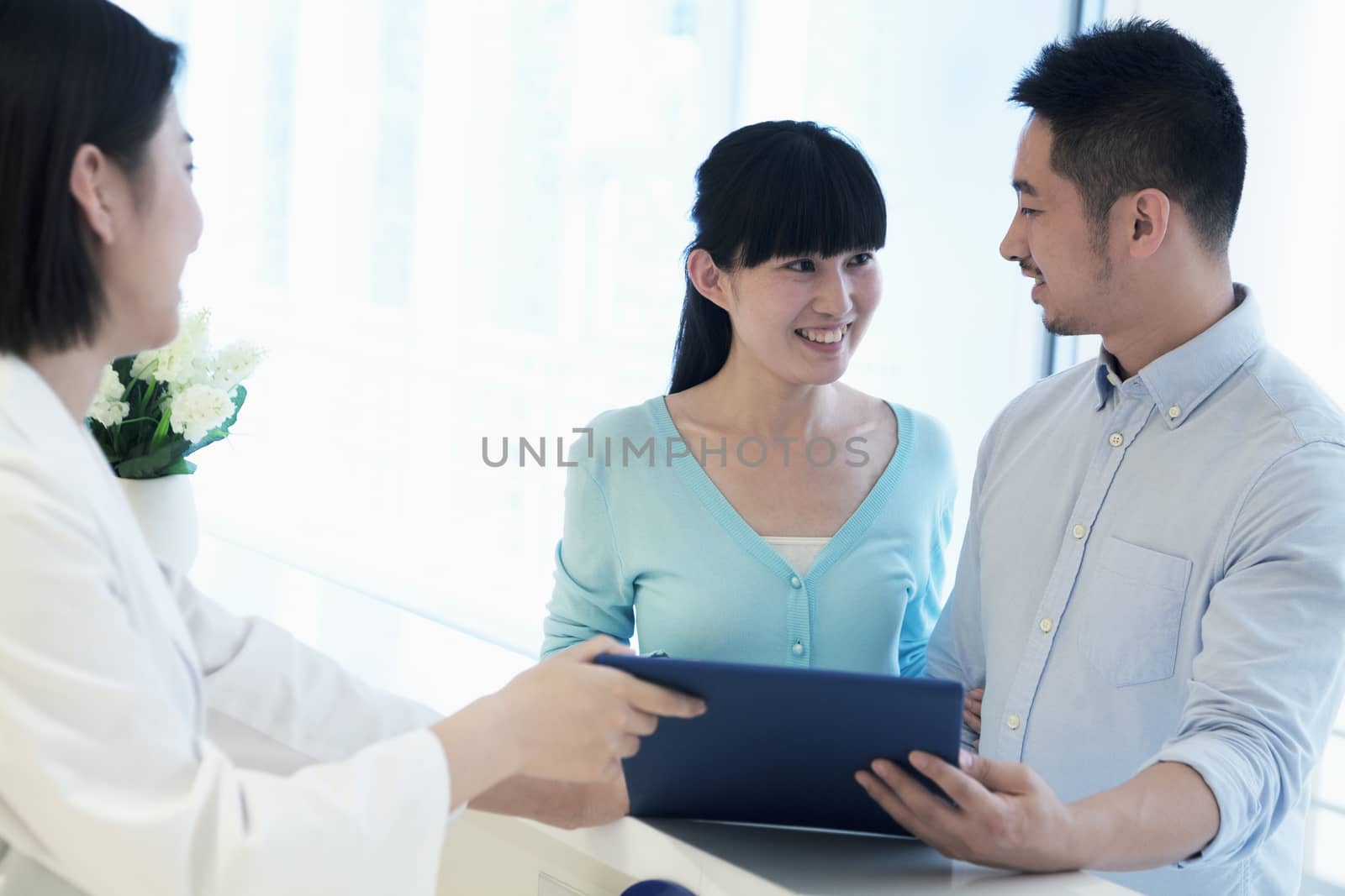 Doctor and smiling couple standing by the counter in the hospital looking at medical record by XiXinXing