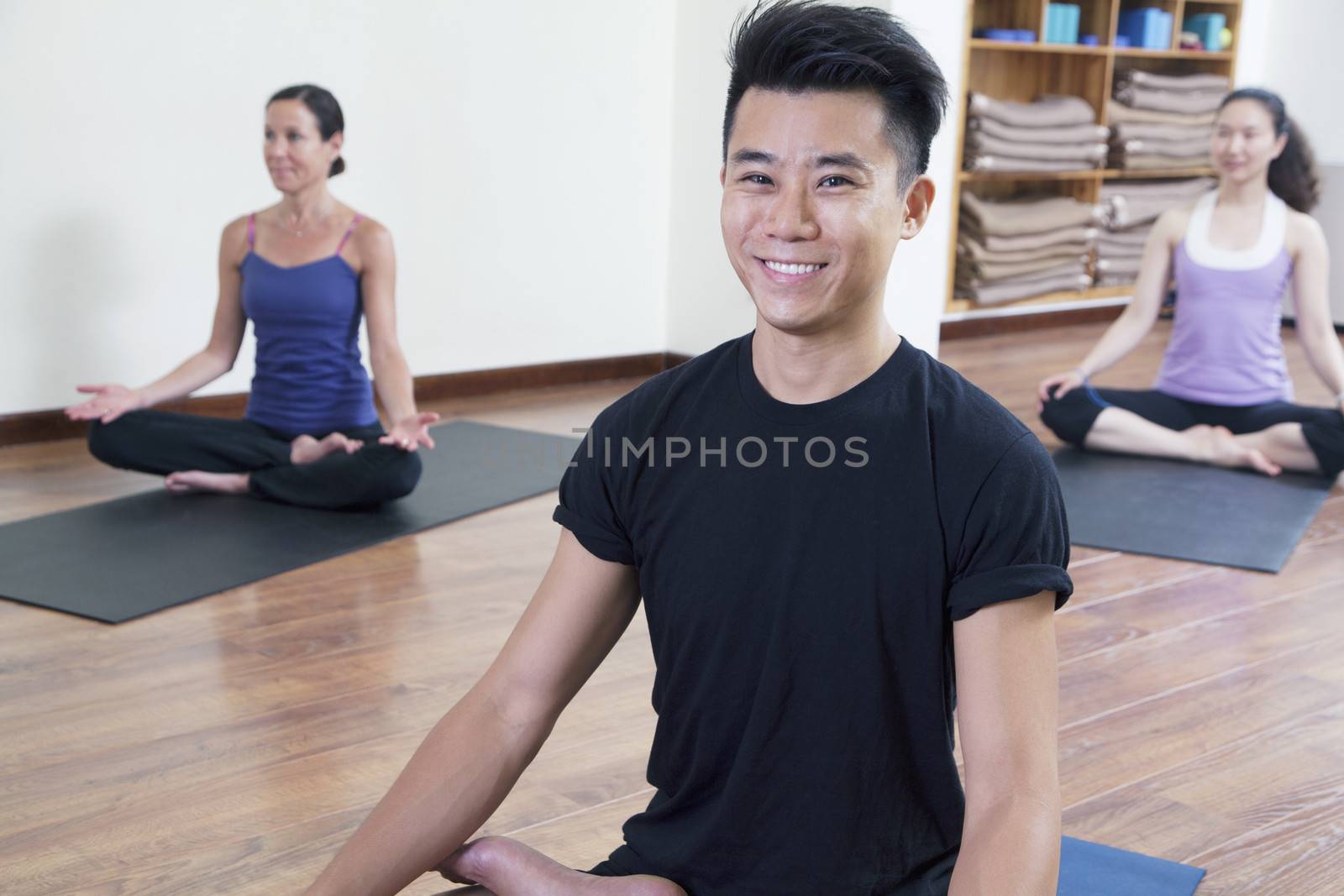 Smiling man sitting cross-legged in a yoga class by XiXinXing