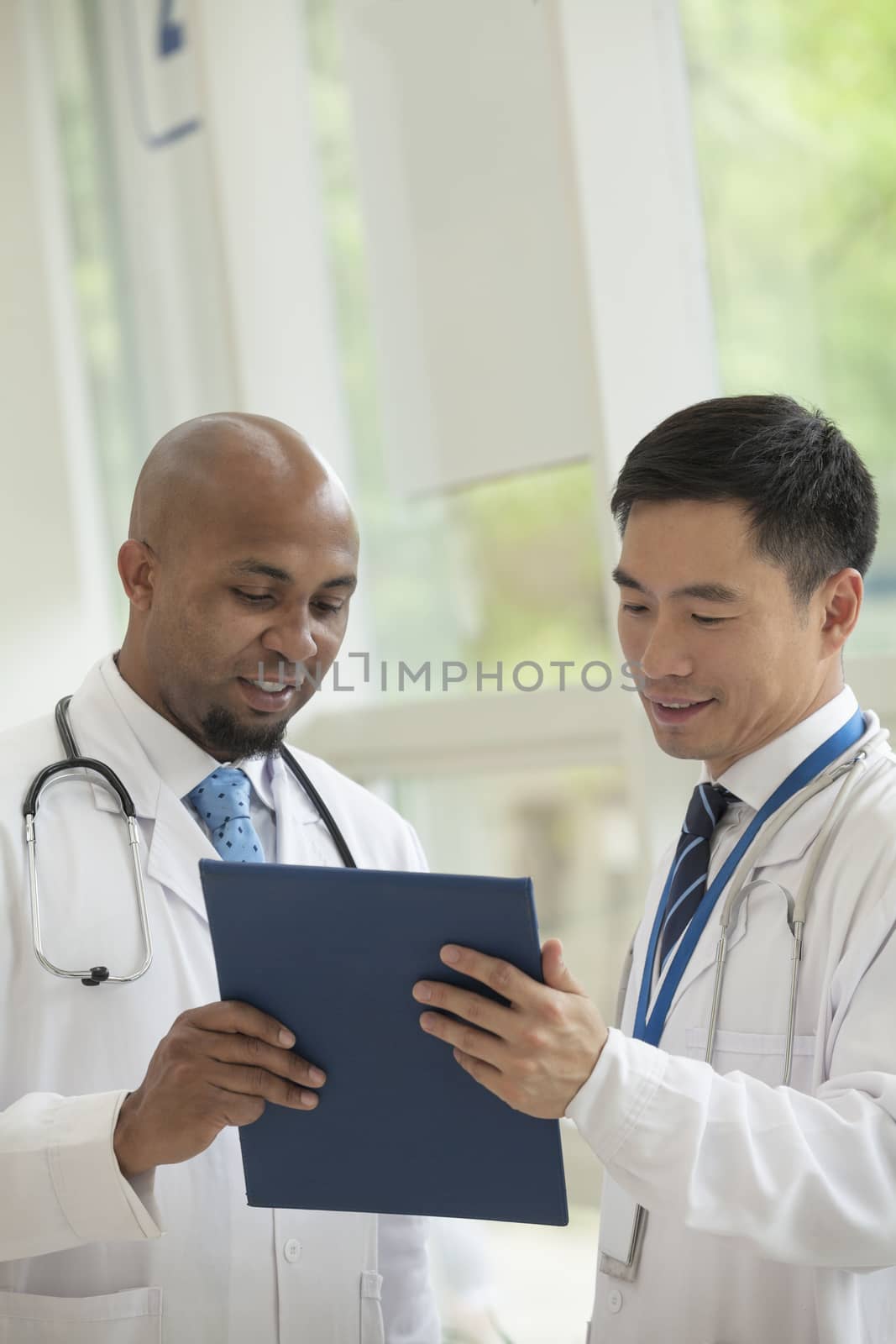 Two doctors looking down and consulting over medical record in the hospital by XiXinXing