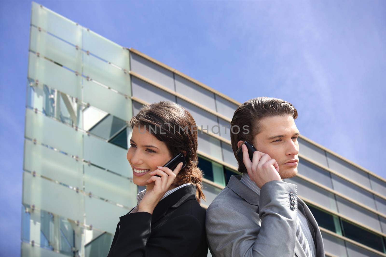 Young business couple using their mobile telephones by phovoir