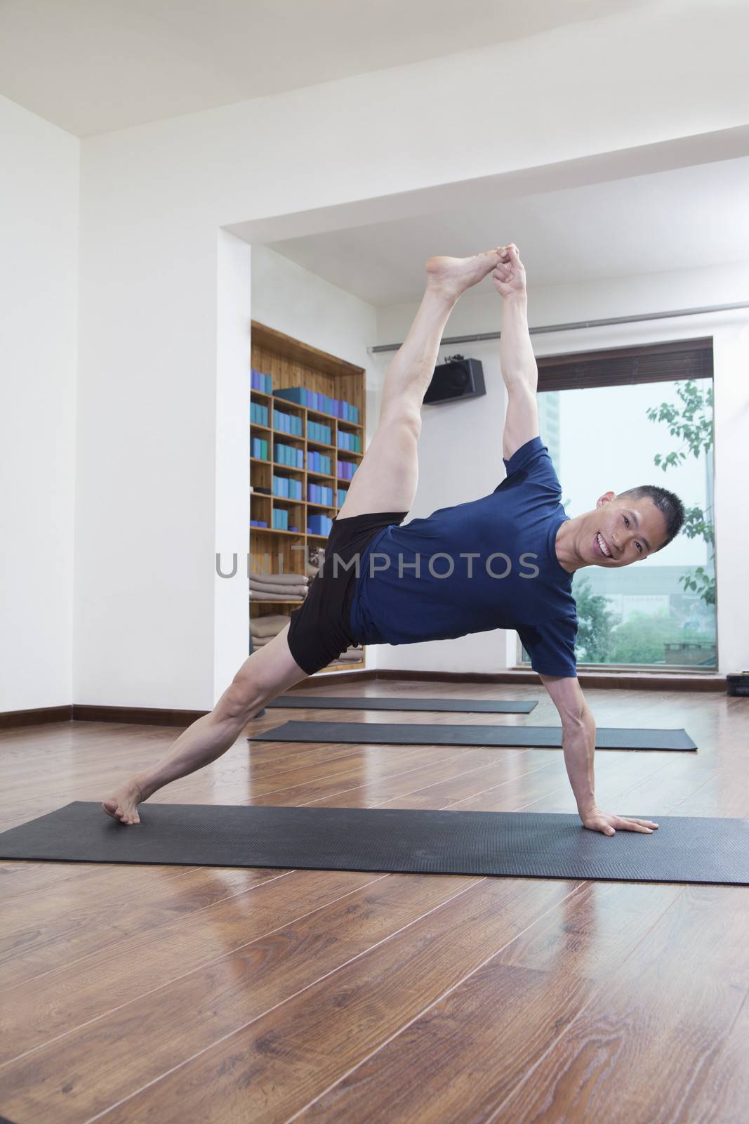 Man with legs raised and arms outstretched doing yoga in a yoga studio