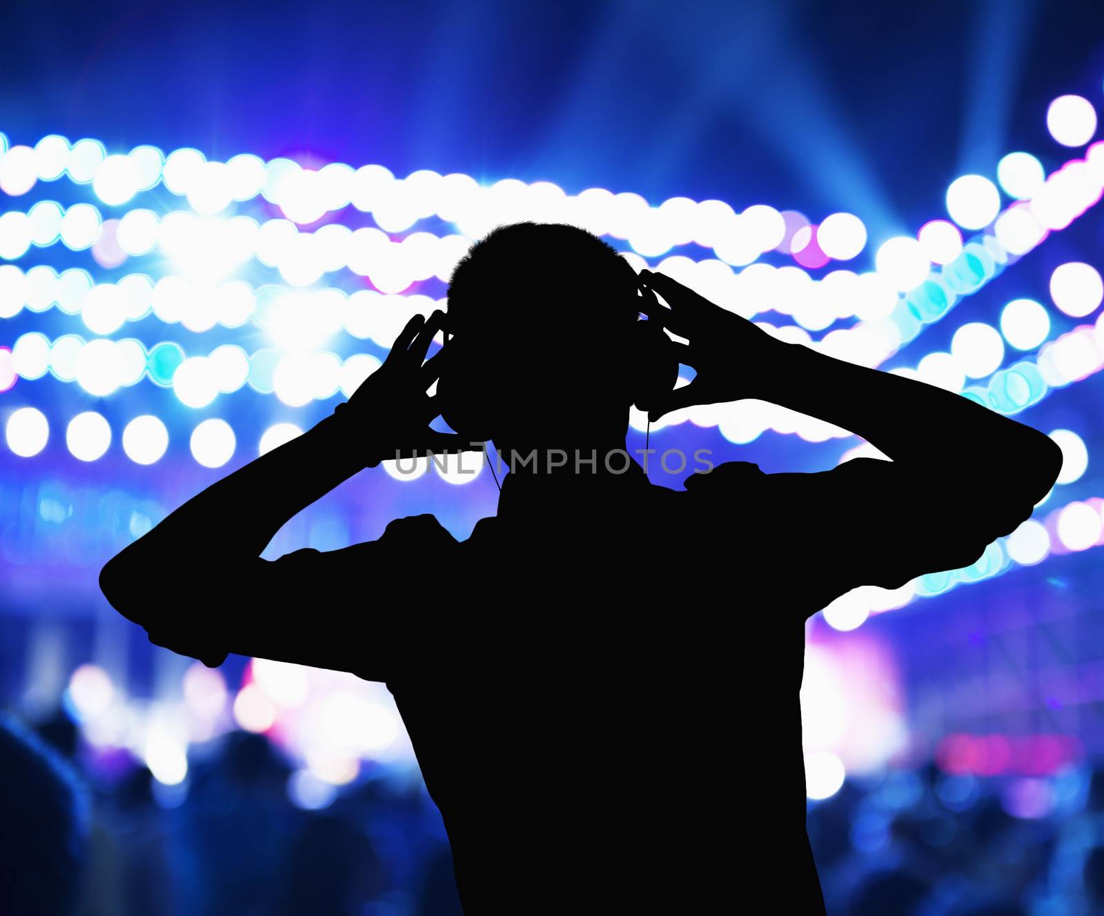 Silhouette of DJ wearing headphones and performing at a night club  by XiXinXing