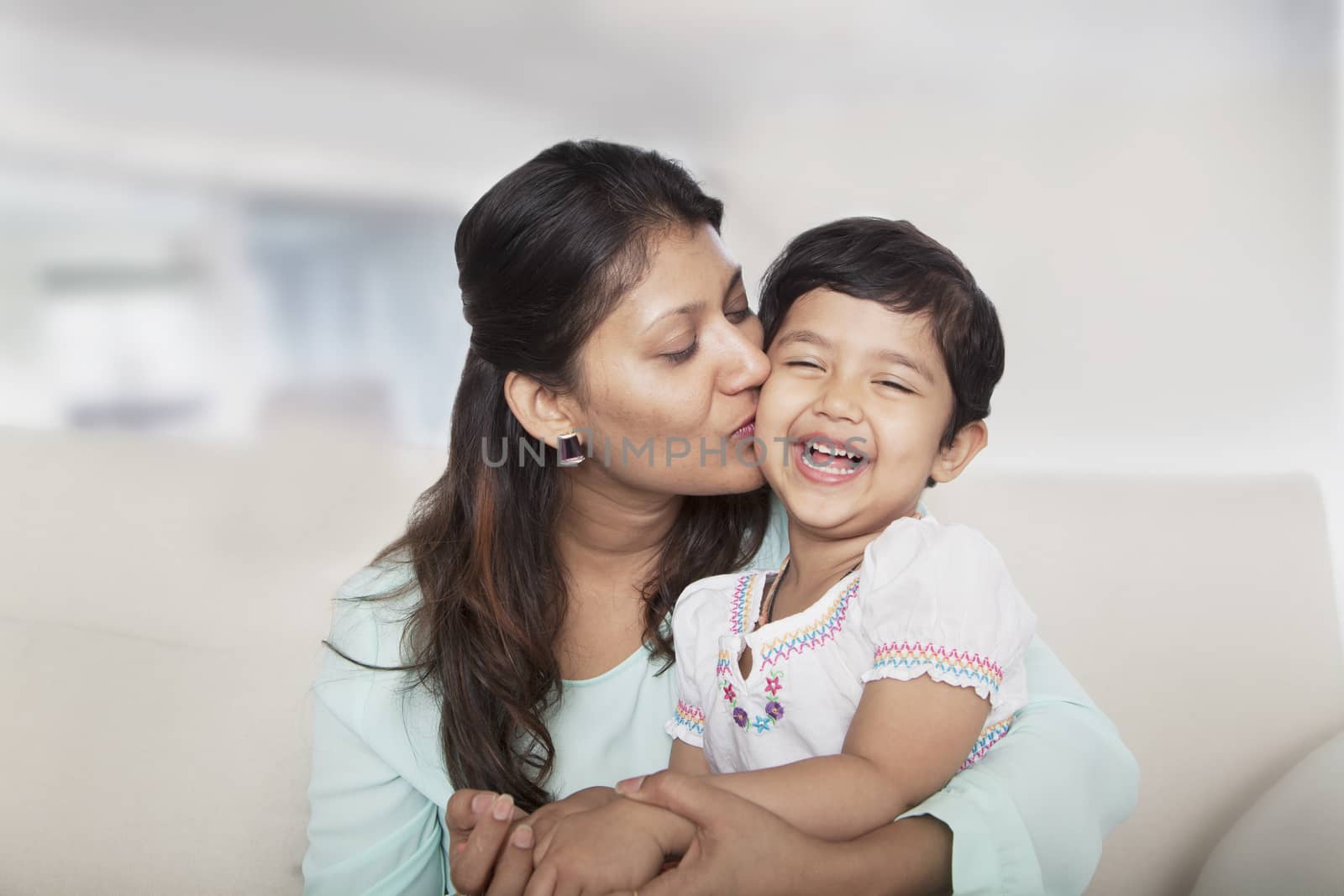 Affectionate mother holding and kissing her daughter on the couch