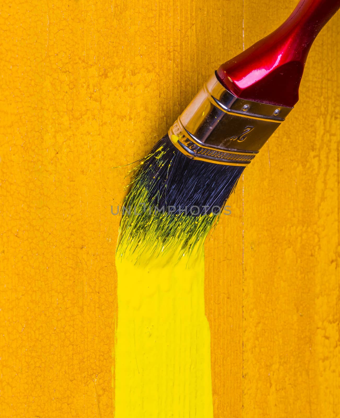 paintbrush with yellow paint dye a wooden wall
