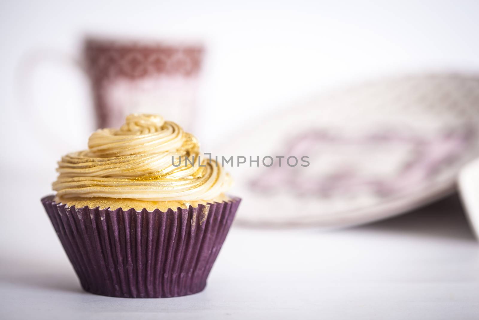 A cupcake in front of plates and a mug, on a white background.