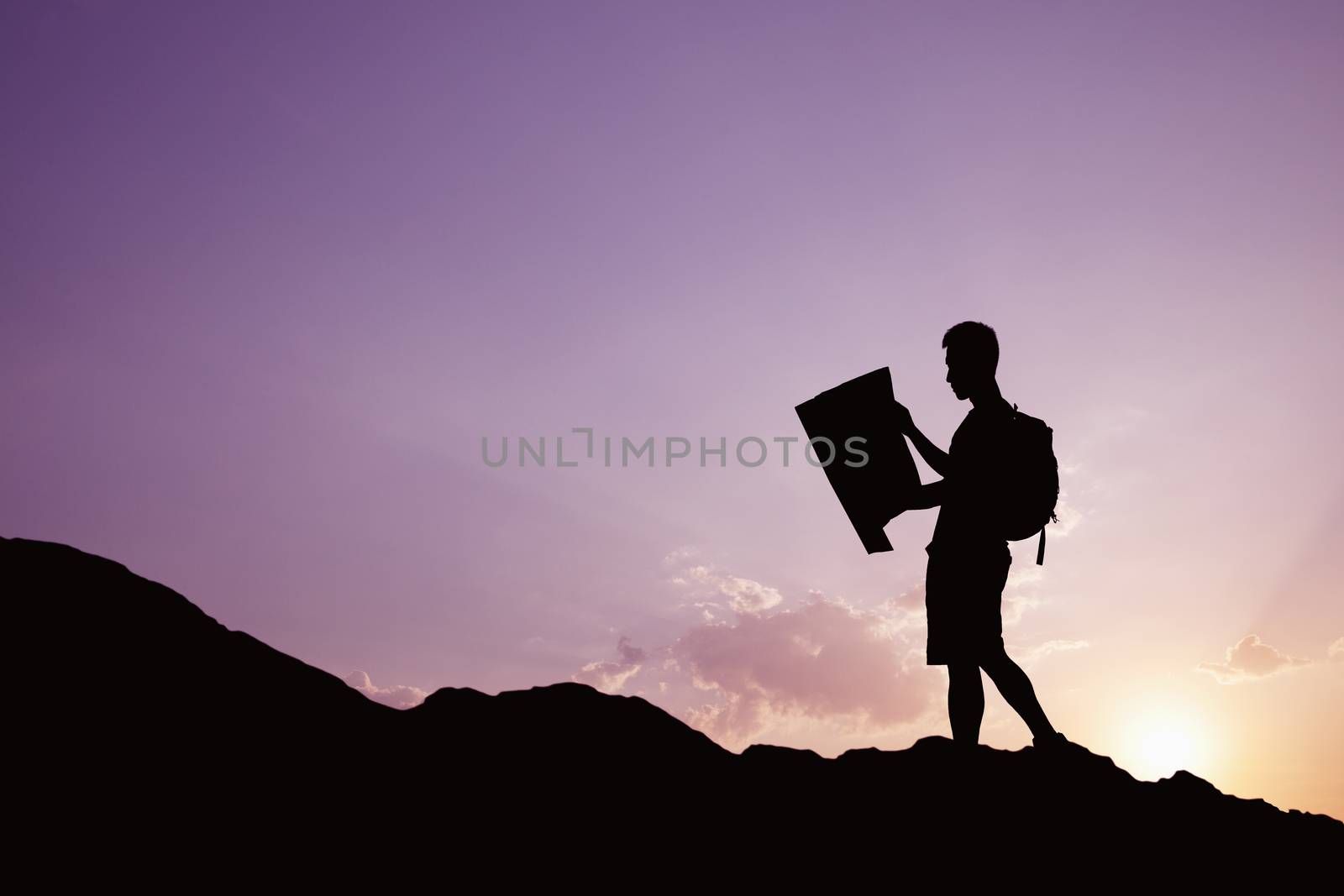 Silhouette of young man looking at a map in nature while hiking by XiXinXing