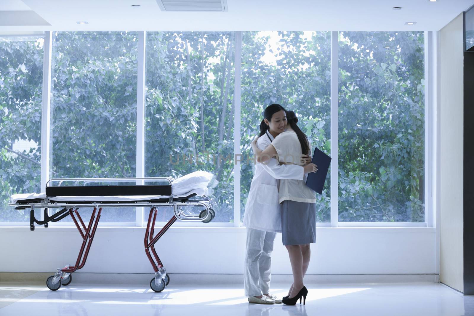 Doctor and patient hugging in a hospital next to a stretcher, full length