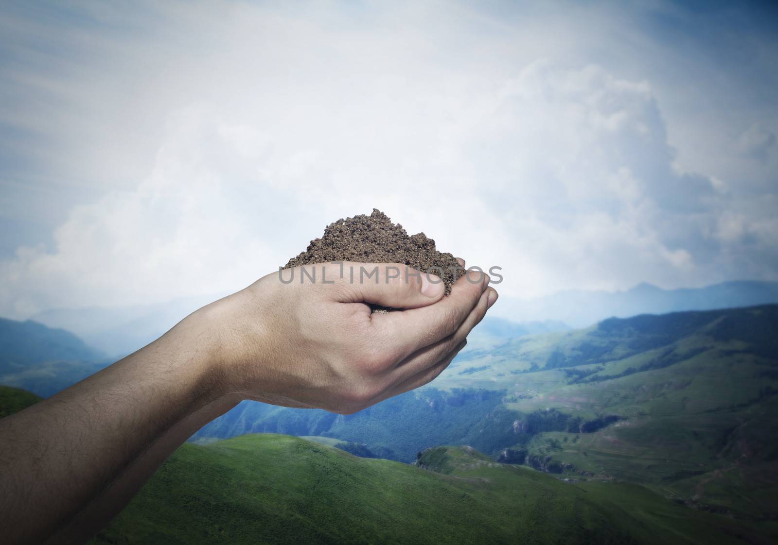 Hands holding a pile of soil with beautiful landscape in the background