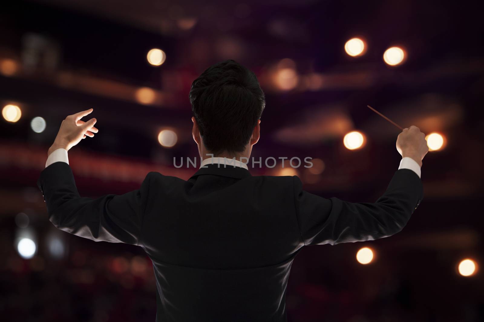Young conductor with baton raised at a performance, rear view  by XiXinXing