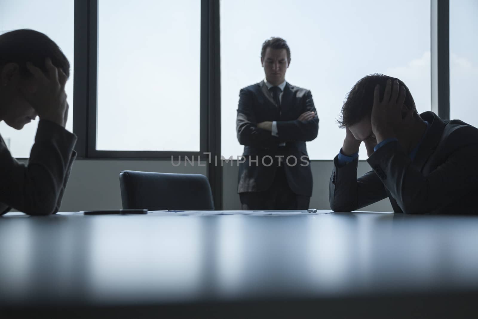 Three frustrated and overworked business people in the board room with arms crossed and head in hands. 