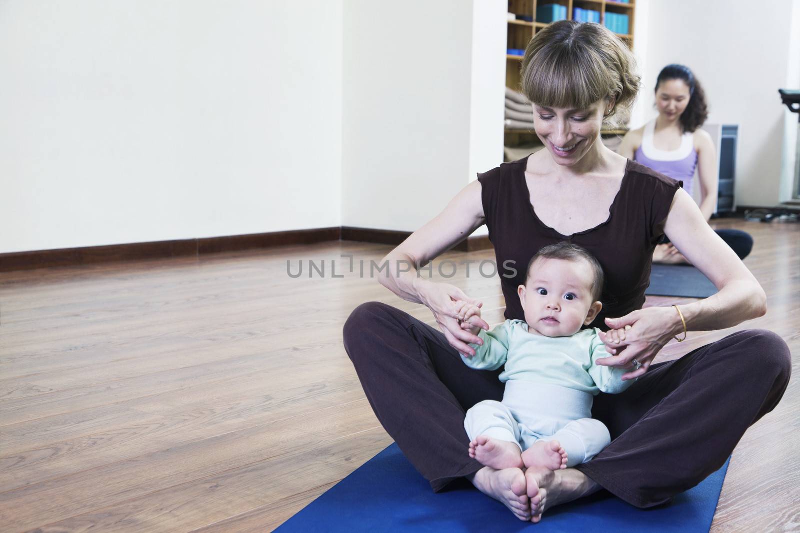 Mother and baby sitting cross-legged and doing yoga in a yoga class by XiXinXing