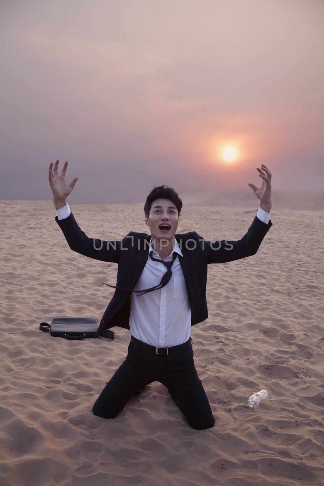 Frustrated businessman with arms outstretched kneeling in the desert at sunset by XiXinXing