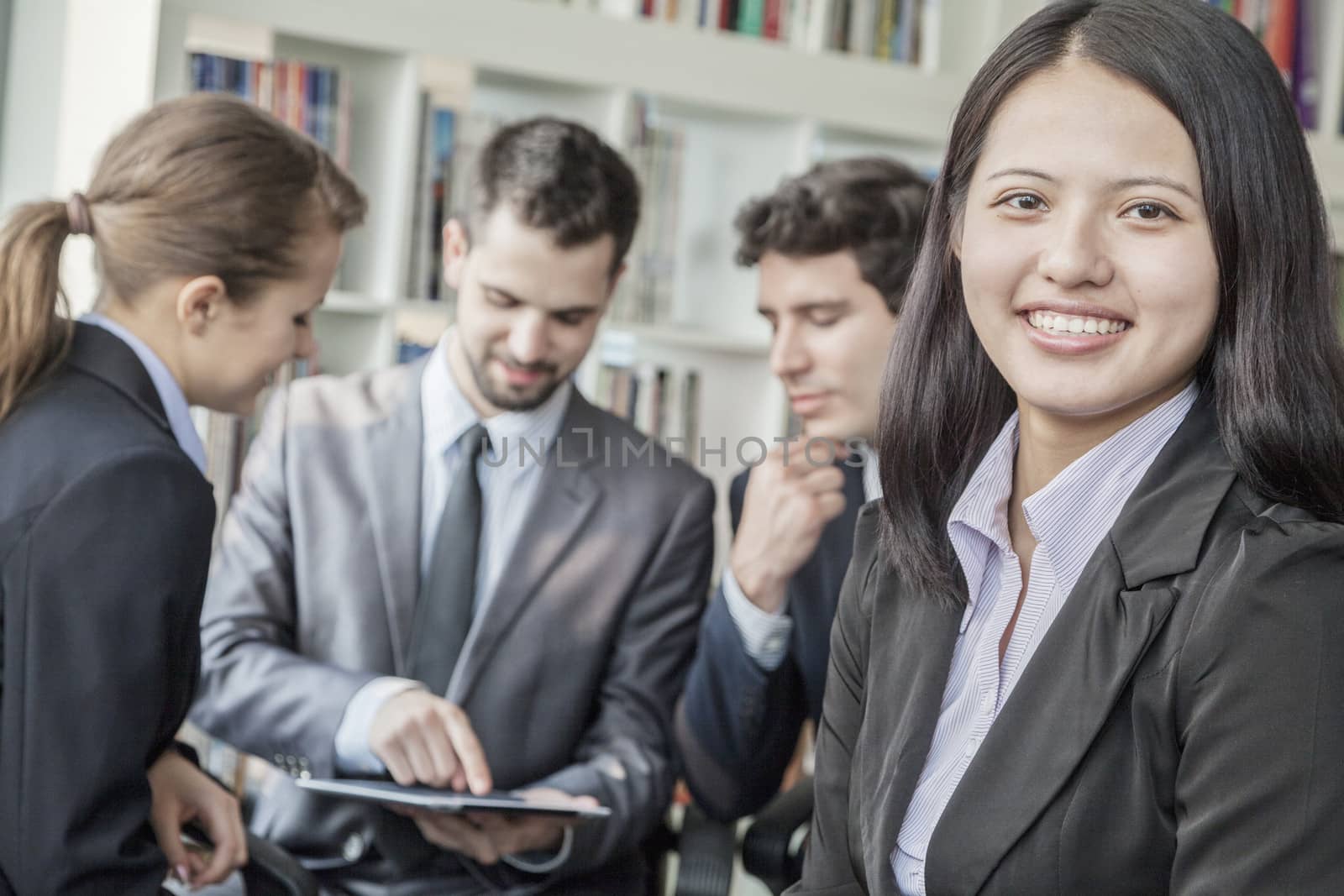 Business woman smiling and looking at the camera with her colleagues talking and looking down at a digital tablet in the background by XiXinXing