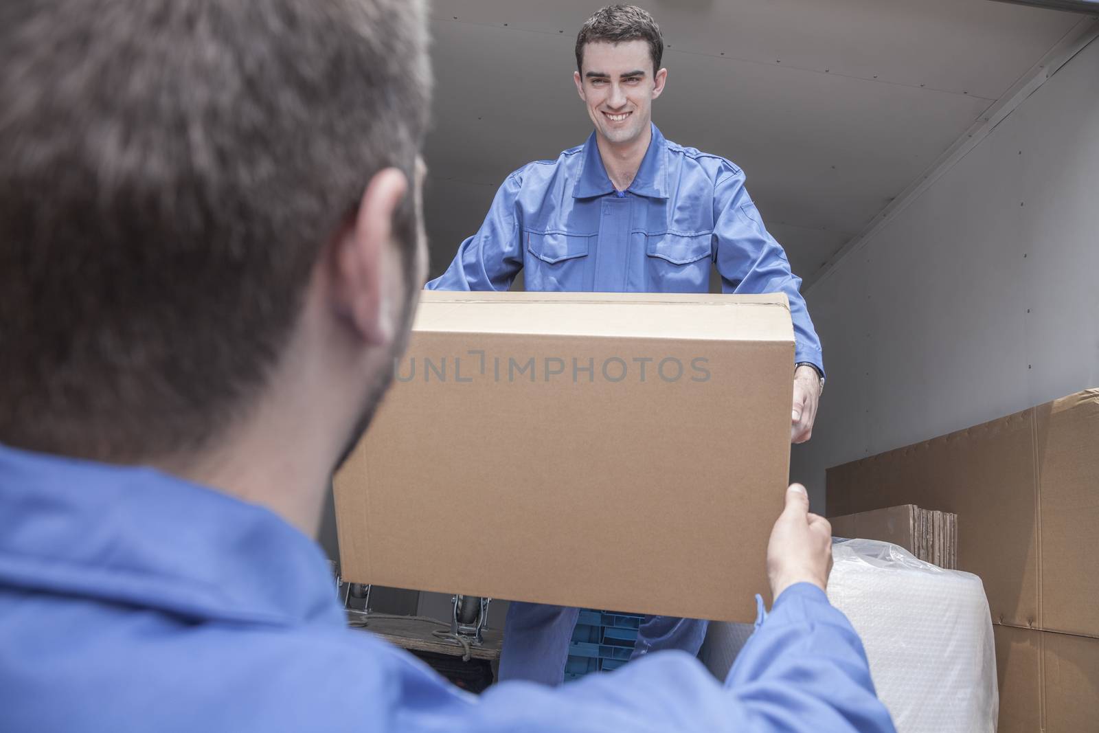 Movers unloading a moving van, passing a cardboard box by XiXinXing