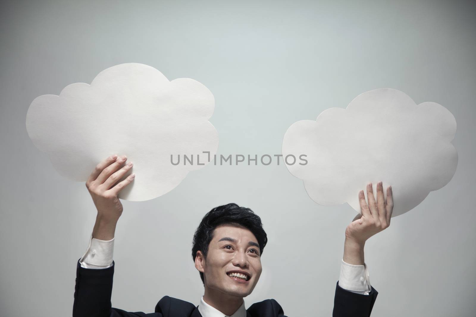 Smiling businessman holding two paper clouds, studio shot