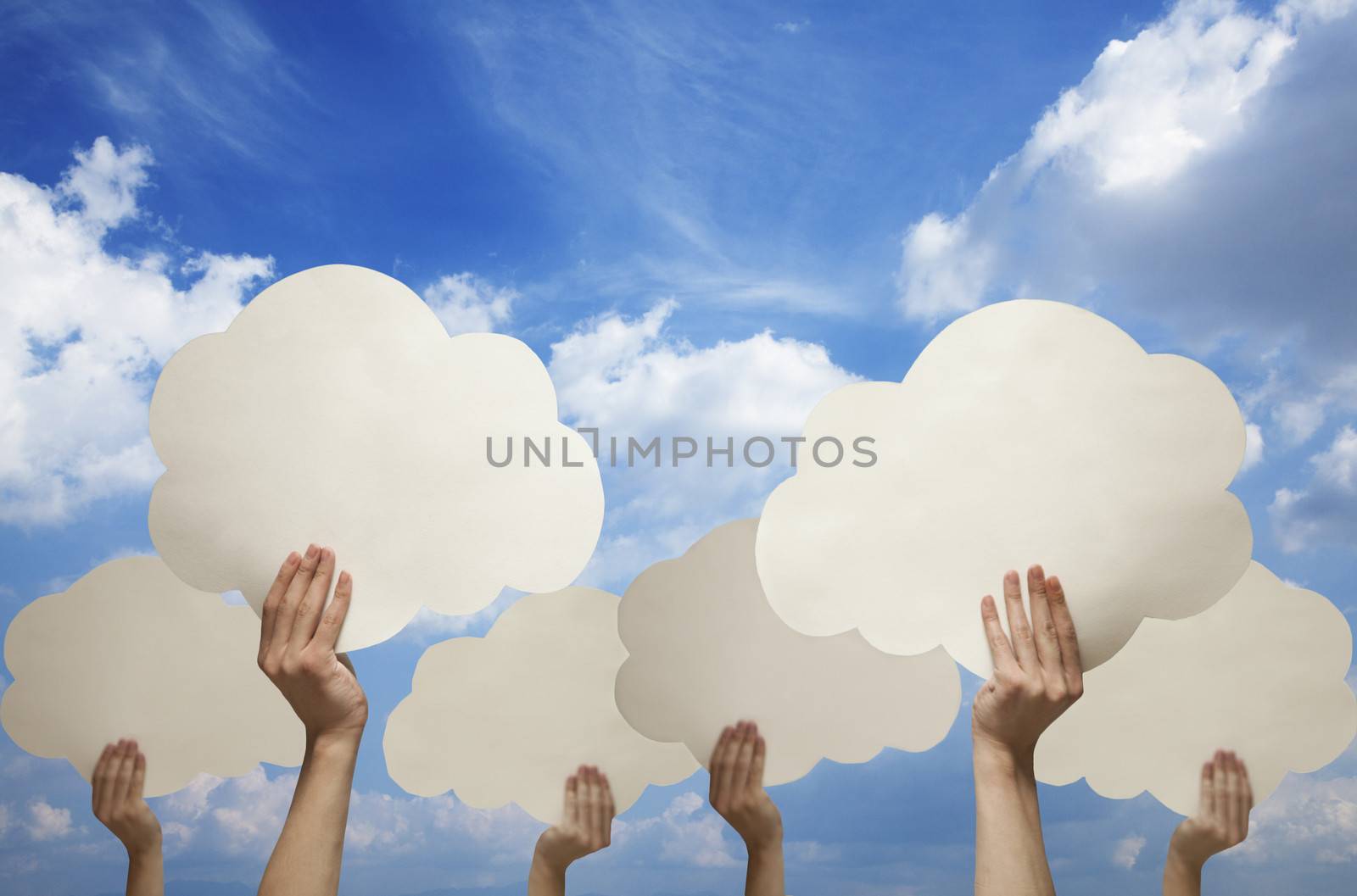 Multiple hands holding cut out paper clouds against a blue sky with clouds