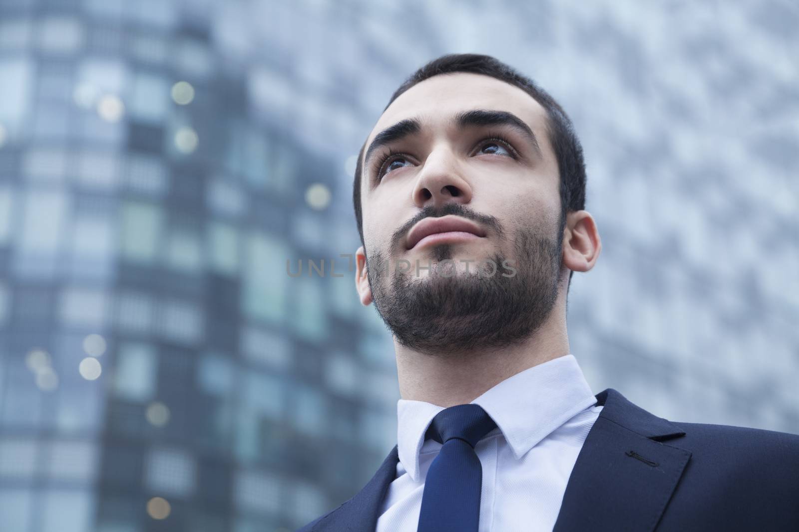 Portrait of serious young businessman looking up, outdoors, business district