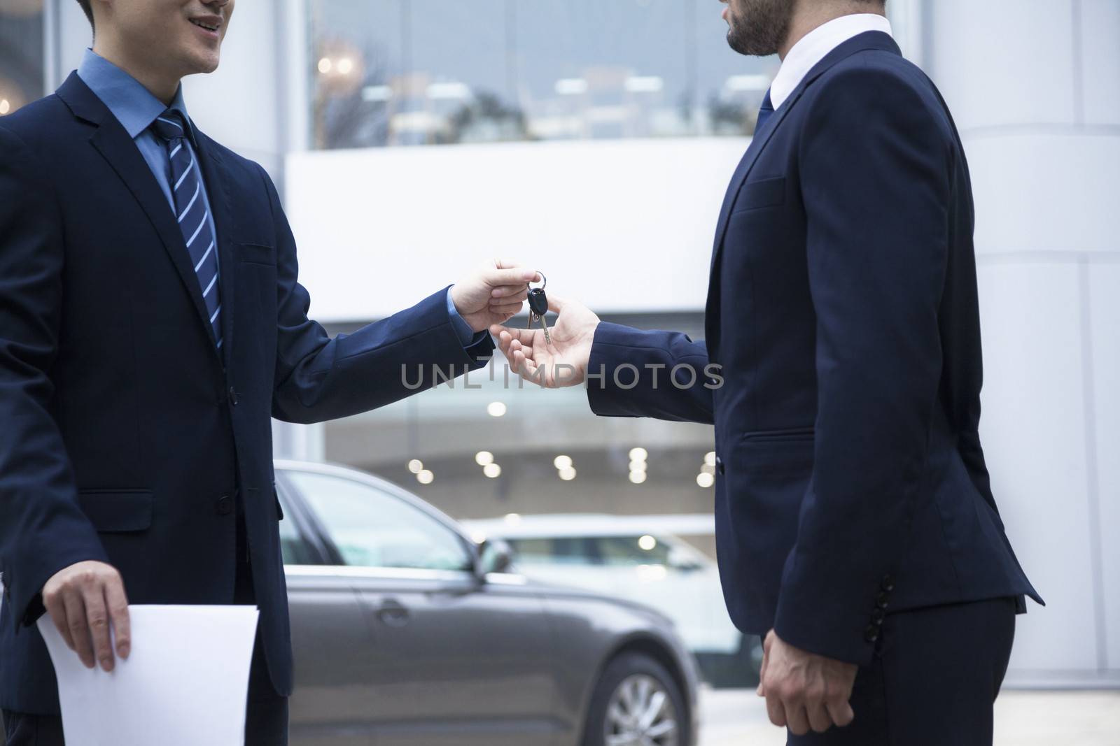 Car salesman handing over the keys for a new car to a young businessman 