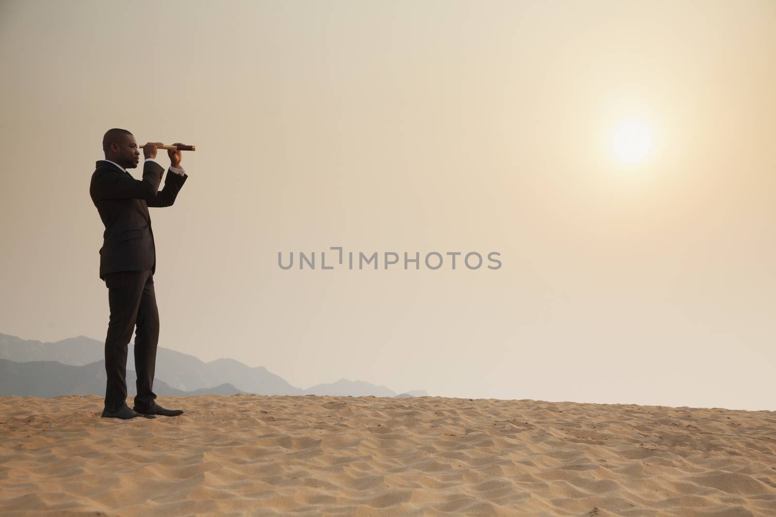 Young businessman looking through telescope in  the middle of the desert