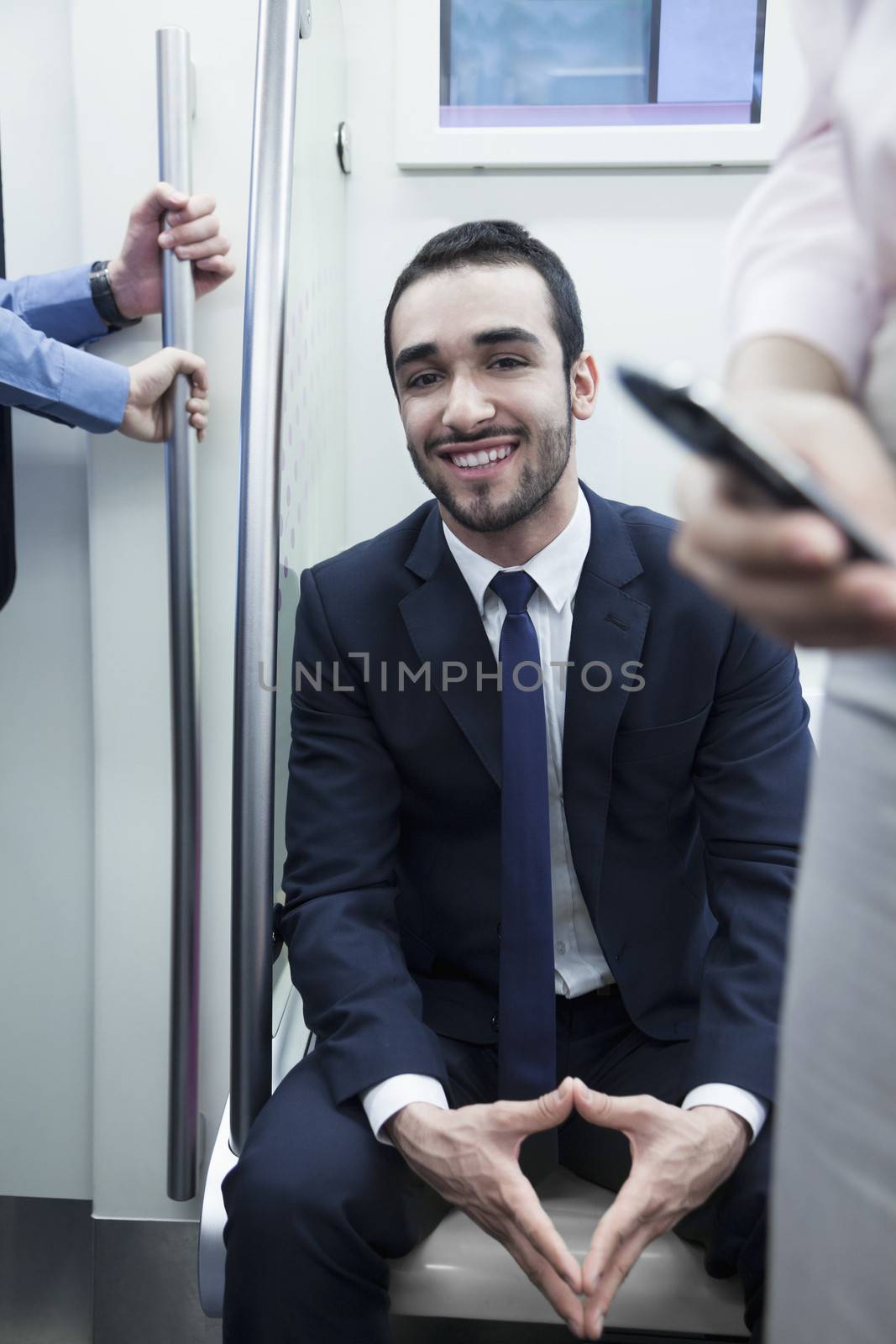 Portrait of young smiling businessman sitting on the subway and looking at camera