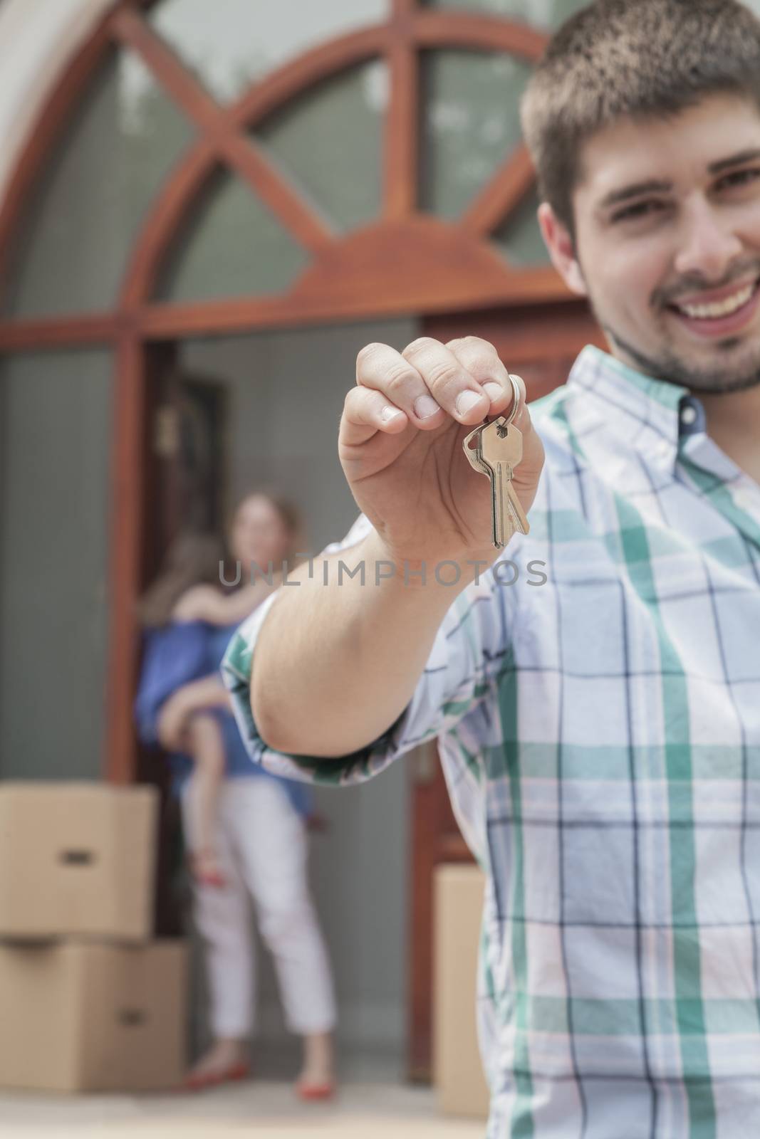 Father smiling and holding the keys to the new house, family in the background