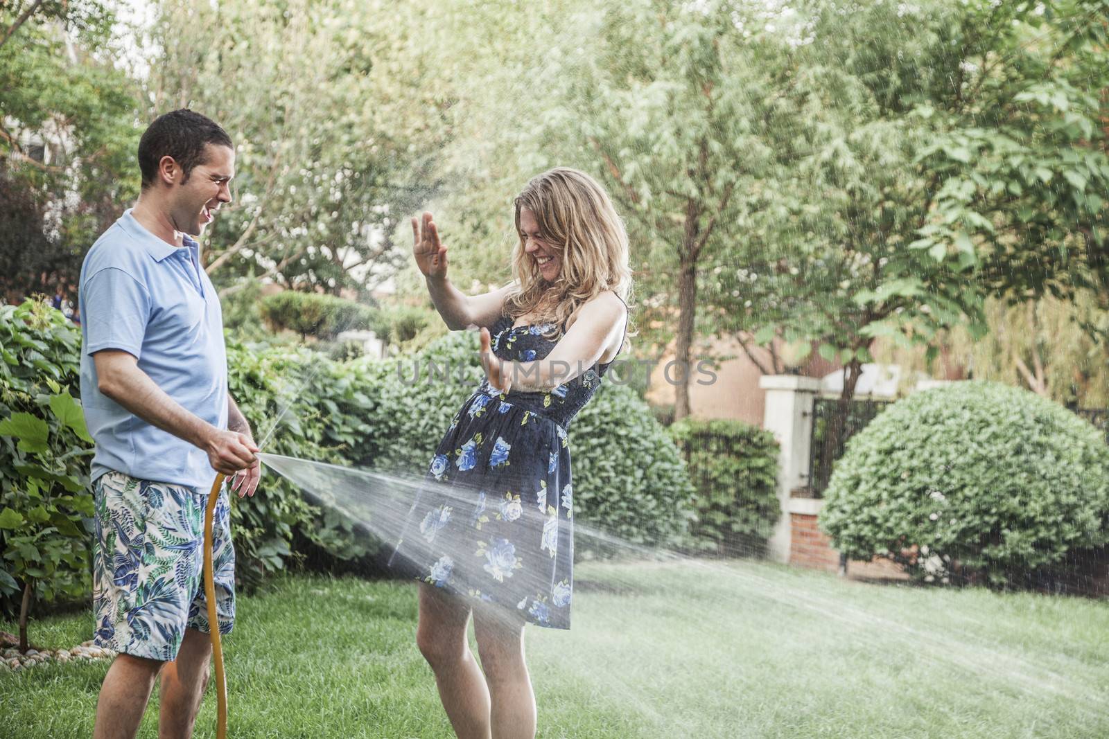 Couple playing with a garden hose and spraying each other outside in the garden  