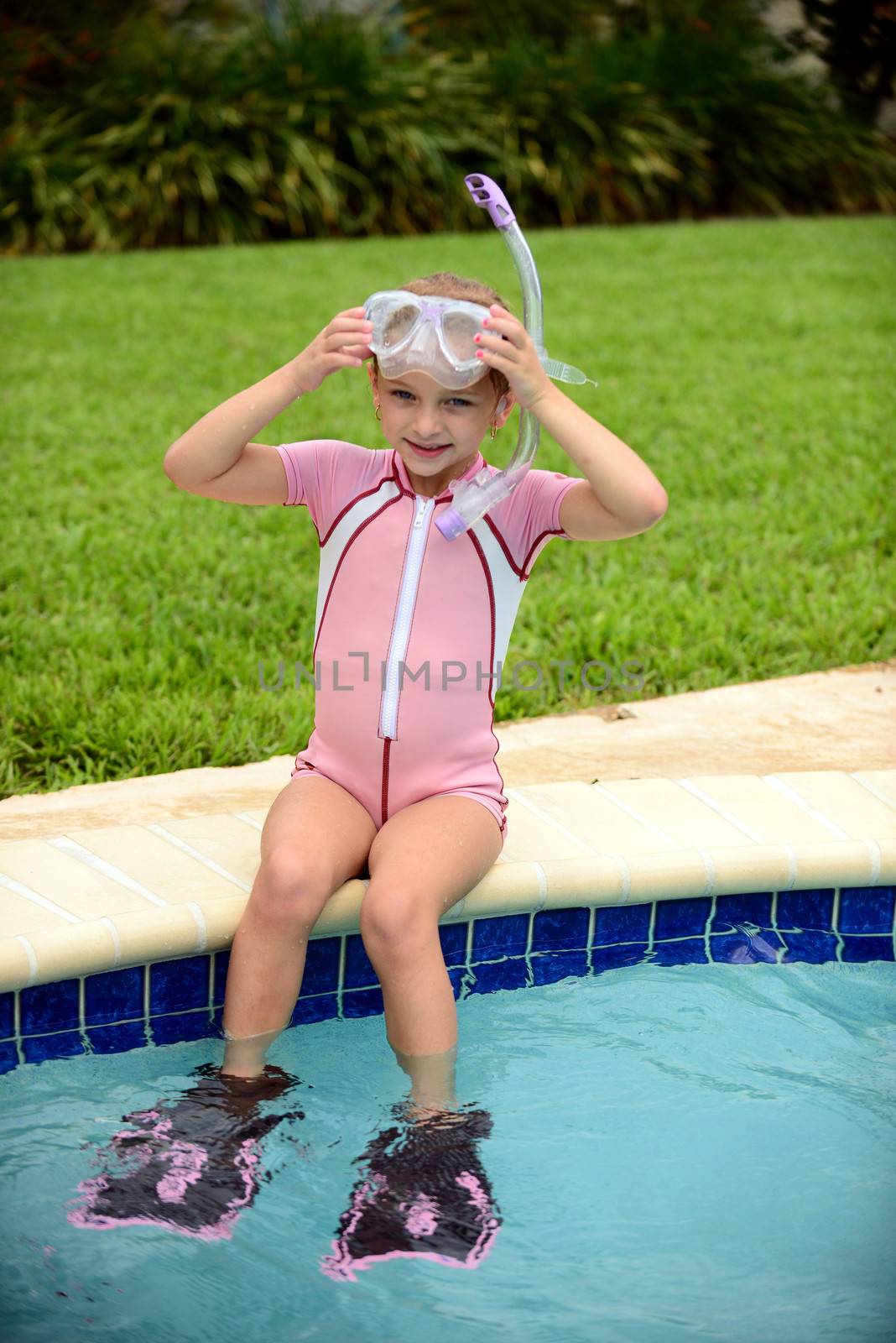 young girl sitting on edge of swimming pool in summer