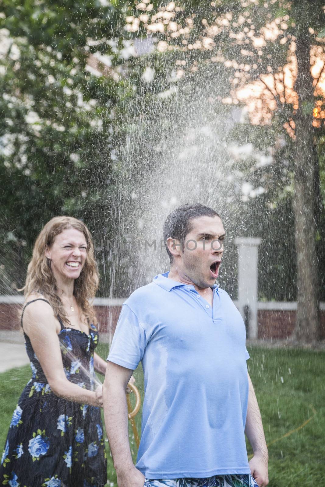 Couple playing with a garden hose and spraying each other outside in the garden, man has a shocked look 