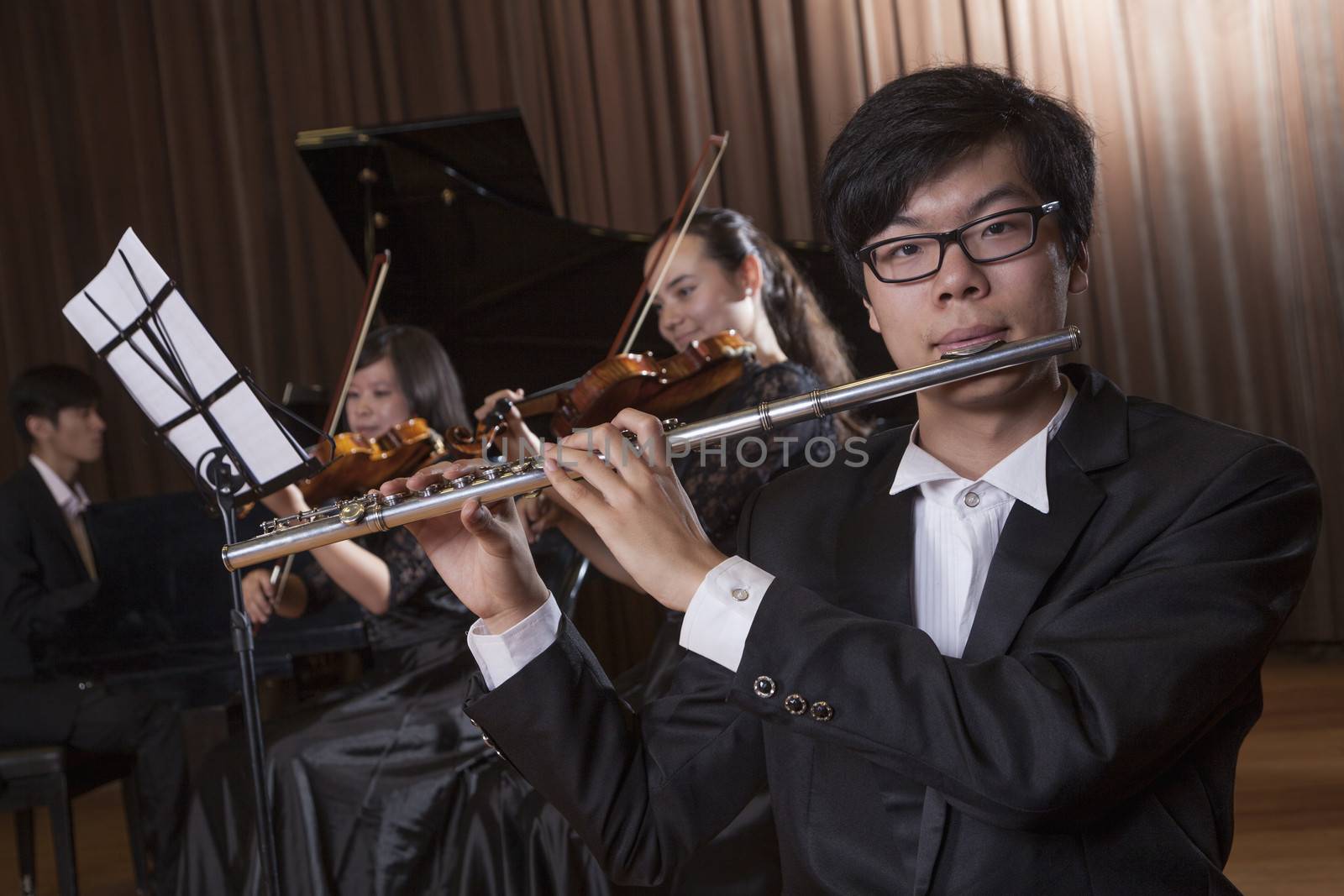 Flautist holding and playing the flute during a performance, looking at the camera by XiXinXing