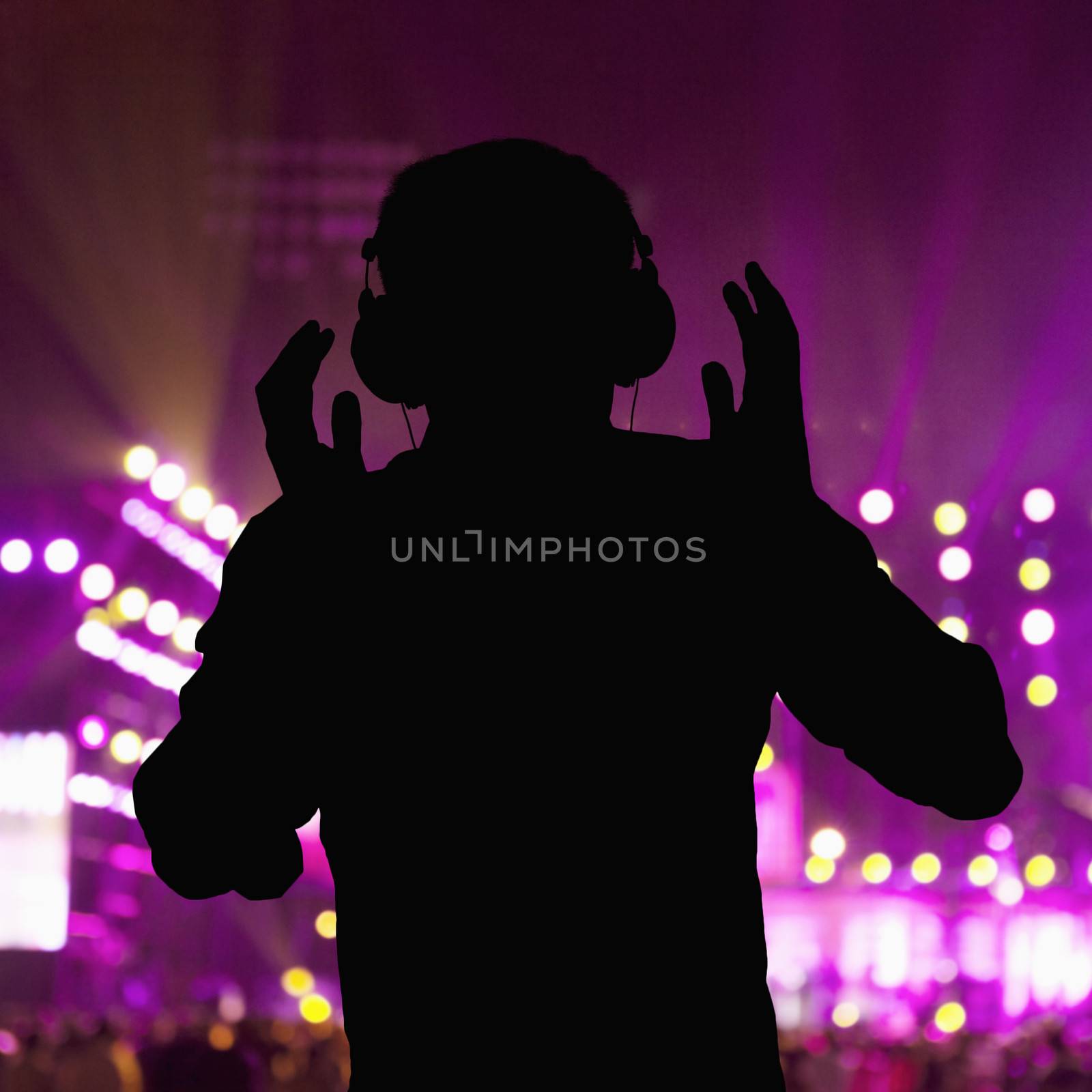 Silhouette of DJ wearing headphones and performing at a night club  by XiXinXing