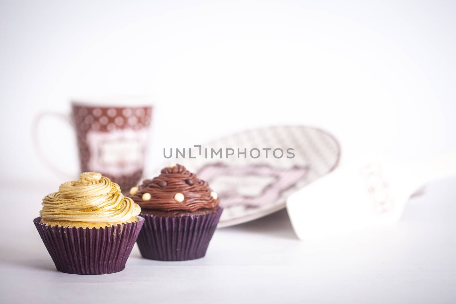 Cupcakes in front of plates and a mug, on a white background.