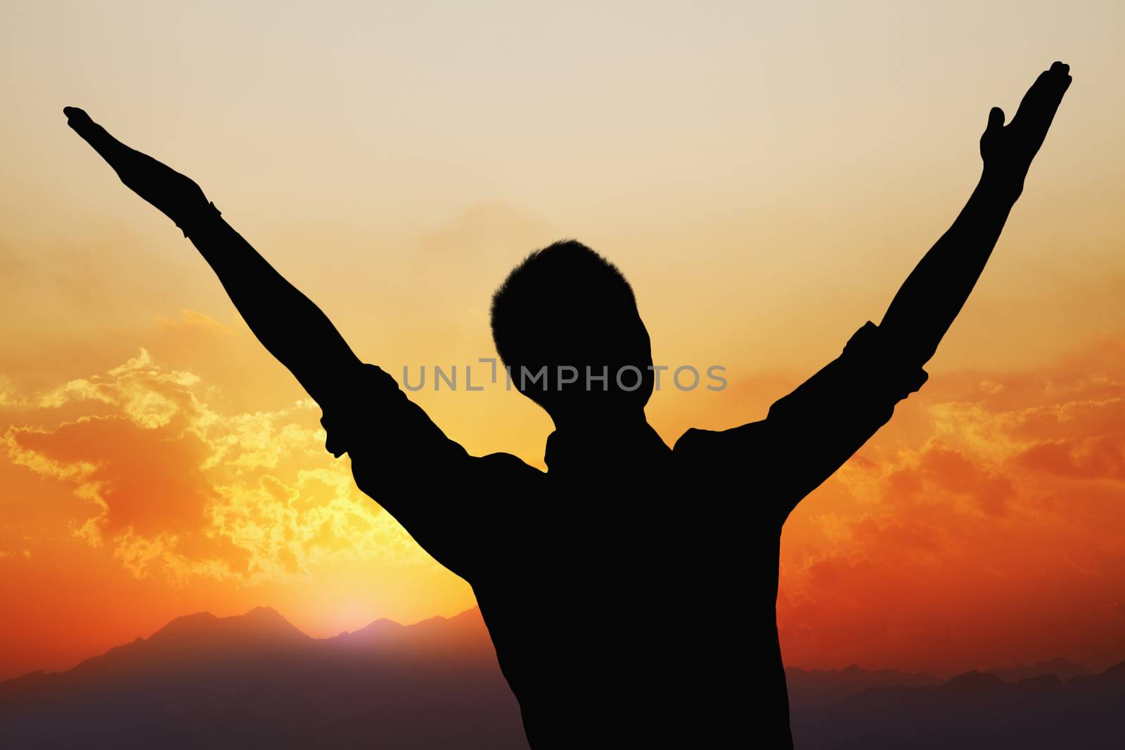Silhouette of young man with arms raised with a beautiful sunset and landscape in the background