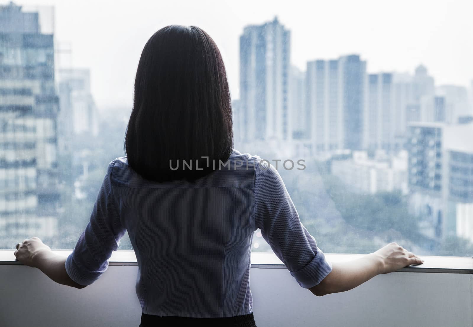 Rear view of a businesswoman looking out the window at the cityscape in Beijing, China by XiXinXing