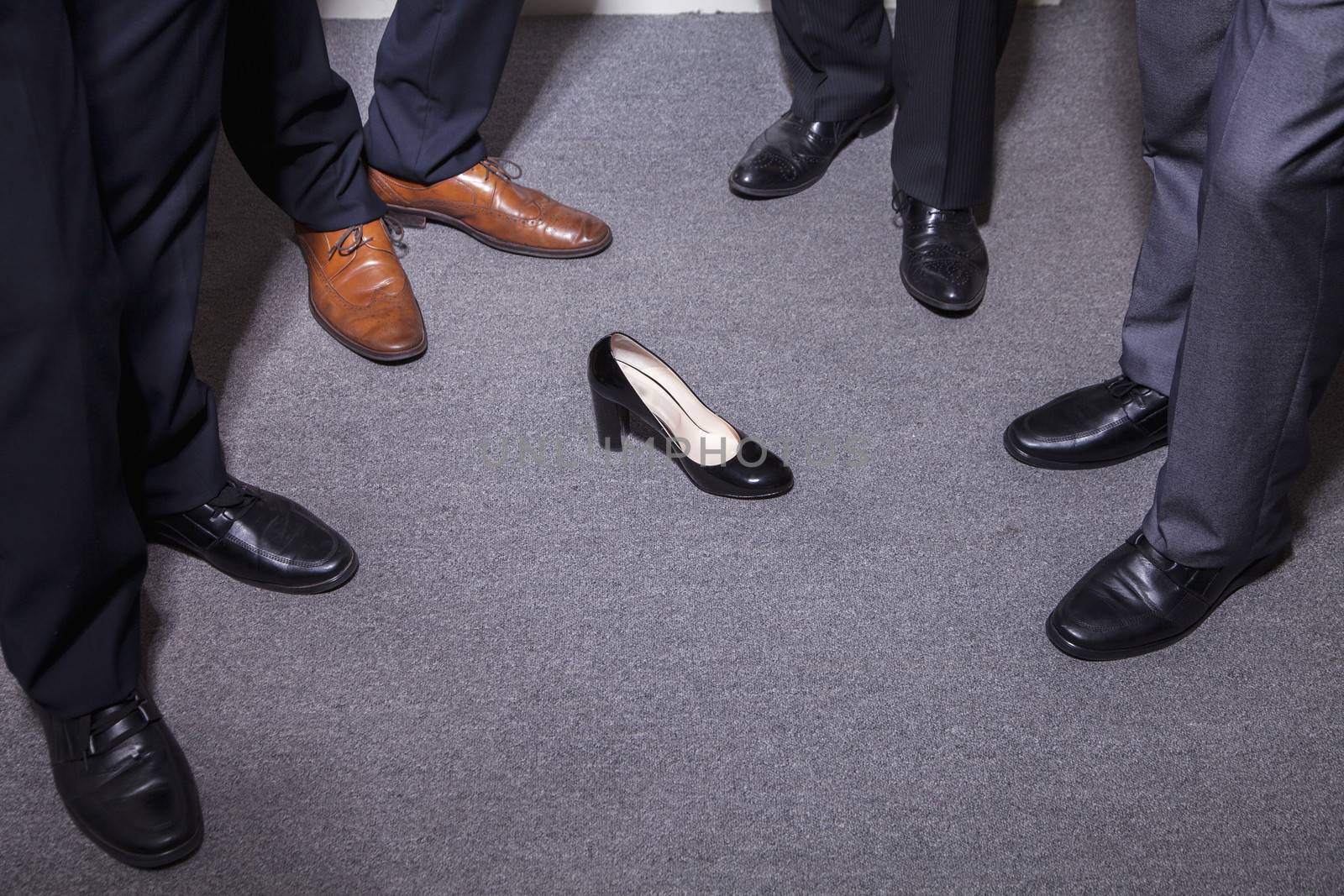 Businessmen standing in a circle around a woman's high heel, feet and legs only