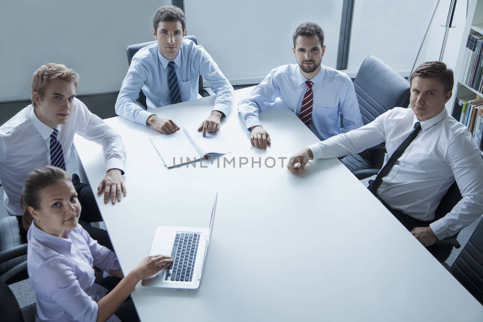 Five business people having a business meeting at the table in the office, looking at camera
