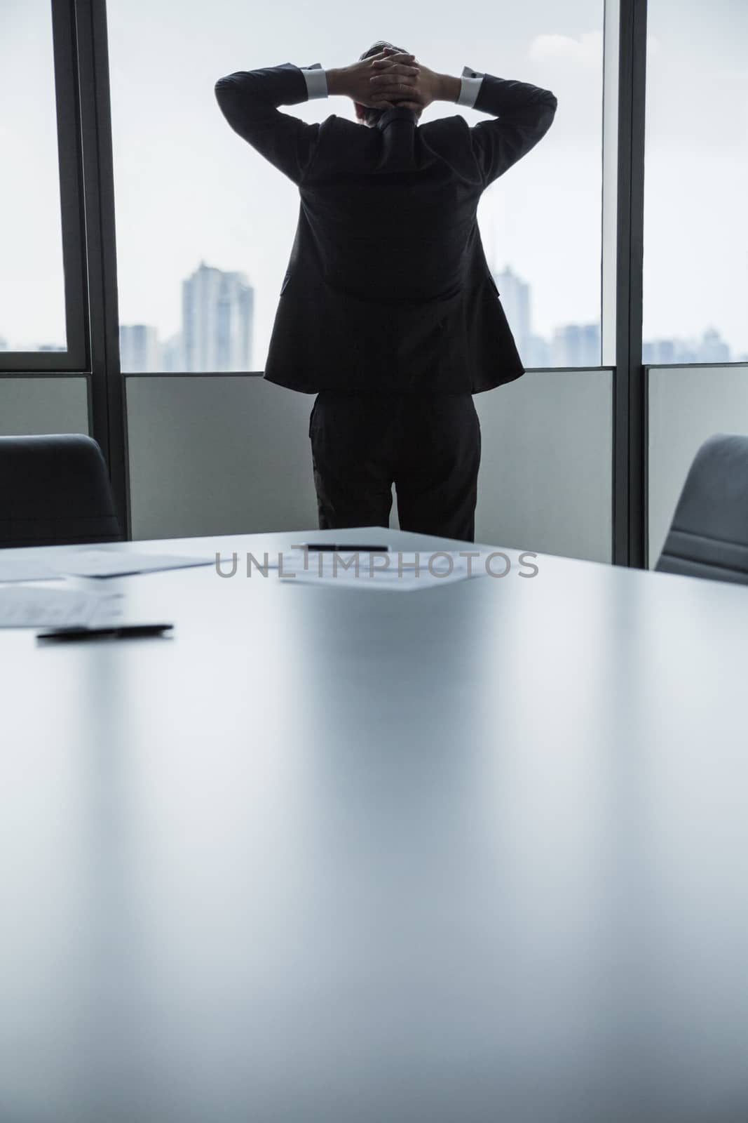 Overworked businessman with hands behind his head looking out the window at the city