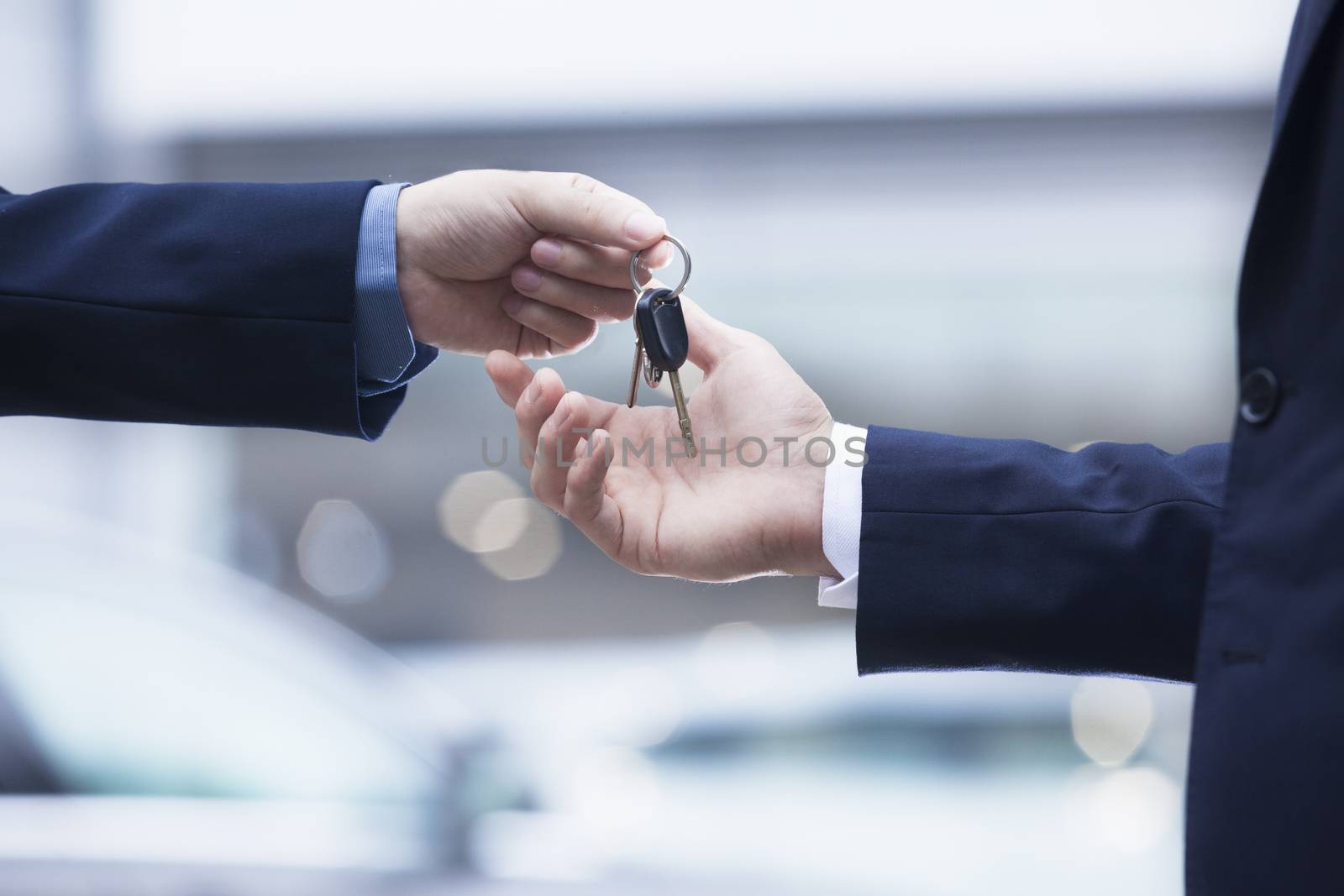 Car salesman handing over the keys for a new car to a young businessman, close-up  by XiXinXing